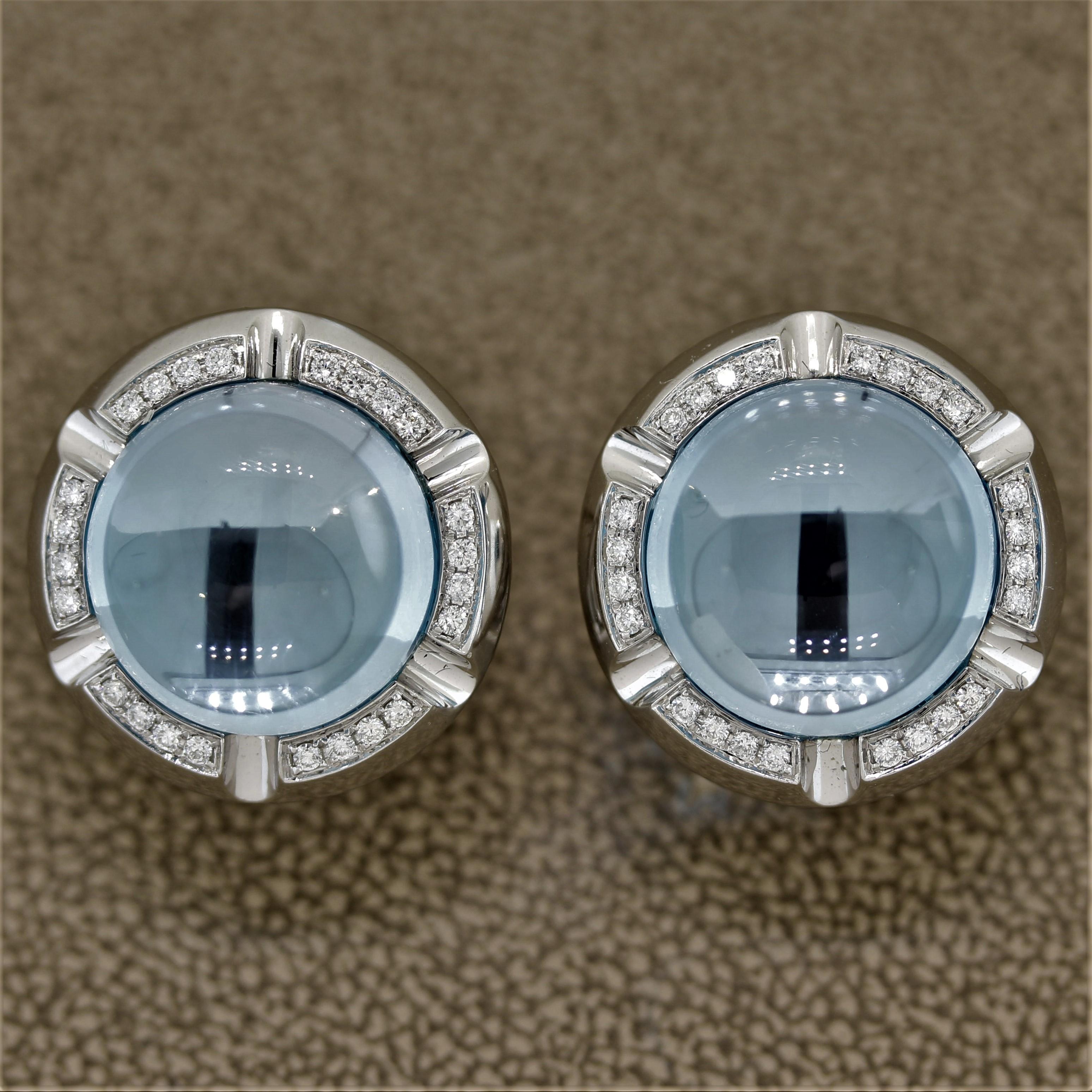 A modern take on the classic button earrings. They feature 24.70 carats of fine blue topaz which match perfectly in color, size, and shape. They are accented by 0.62 carats of round brilliant cut diamonds which are set around the topaz. Made in 18k