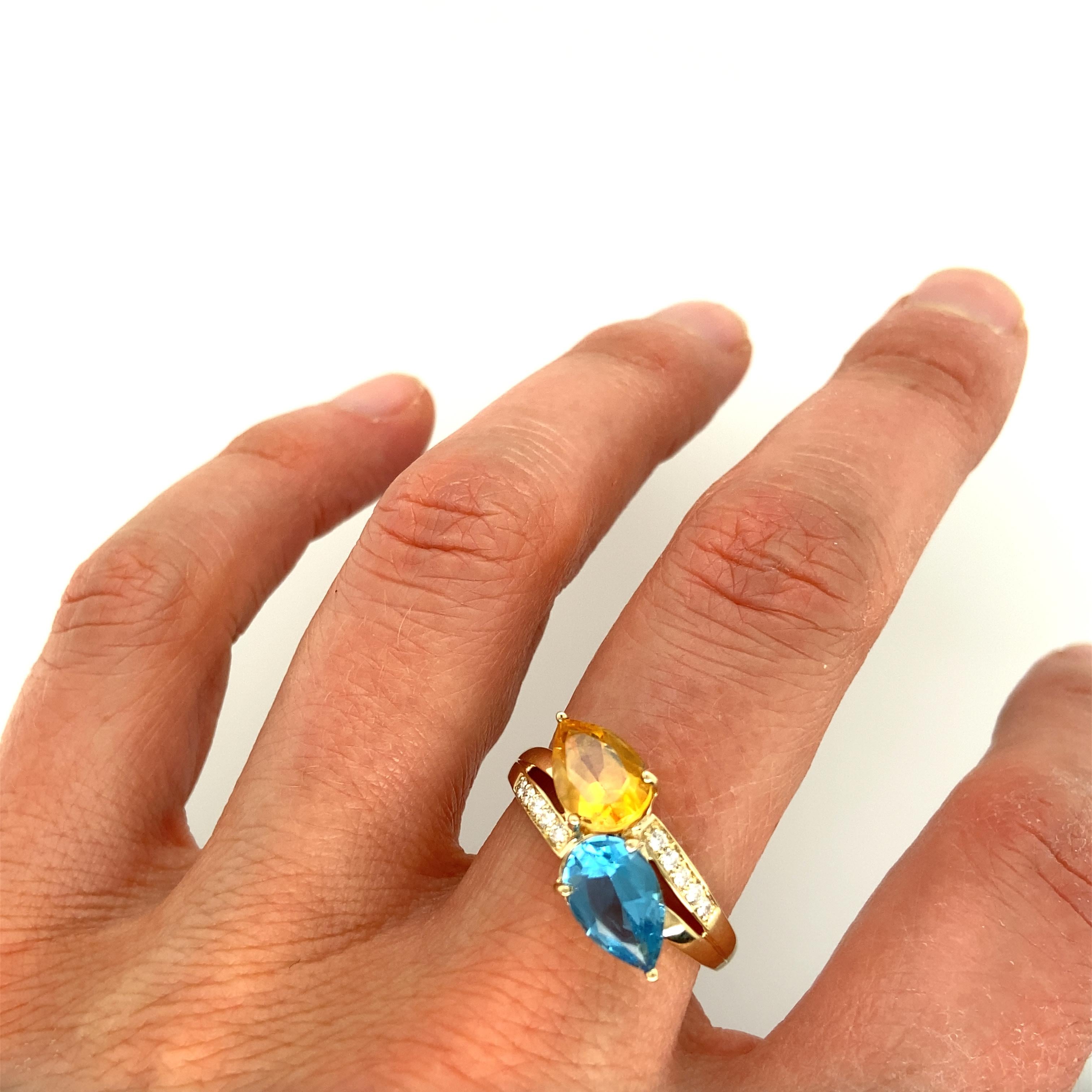 One 14 karat yellow gold ring set with one 9x6.5mm pear shaped blue topaz, one 9x6.5mm pear shaped golden citrine, and ten brilliant cut diamonds, 0.10 carat total weight with matching H/I color and SI clarity.  The shank measures 3.95mm near the