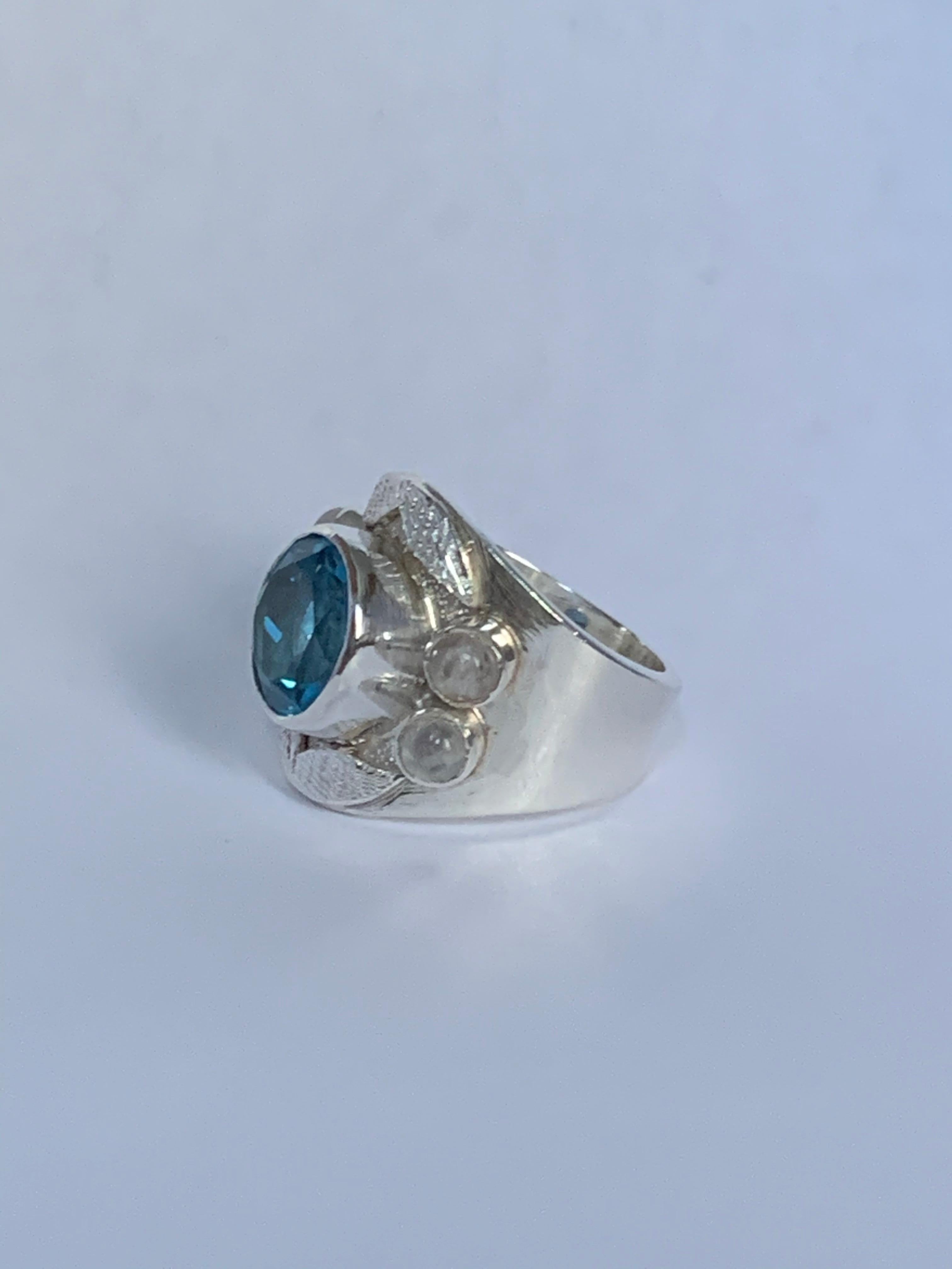 Fabriquée avec soin à la main, cette bague unique en son genre est faite de topaze bleue et de pierre de lune. Le design artistique de la bague marie son audace et sa modernité. Serti en argent sterling. 