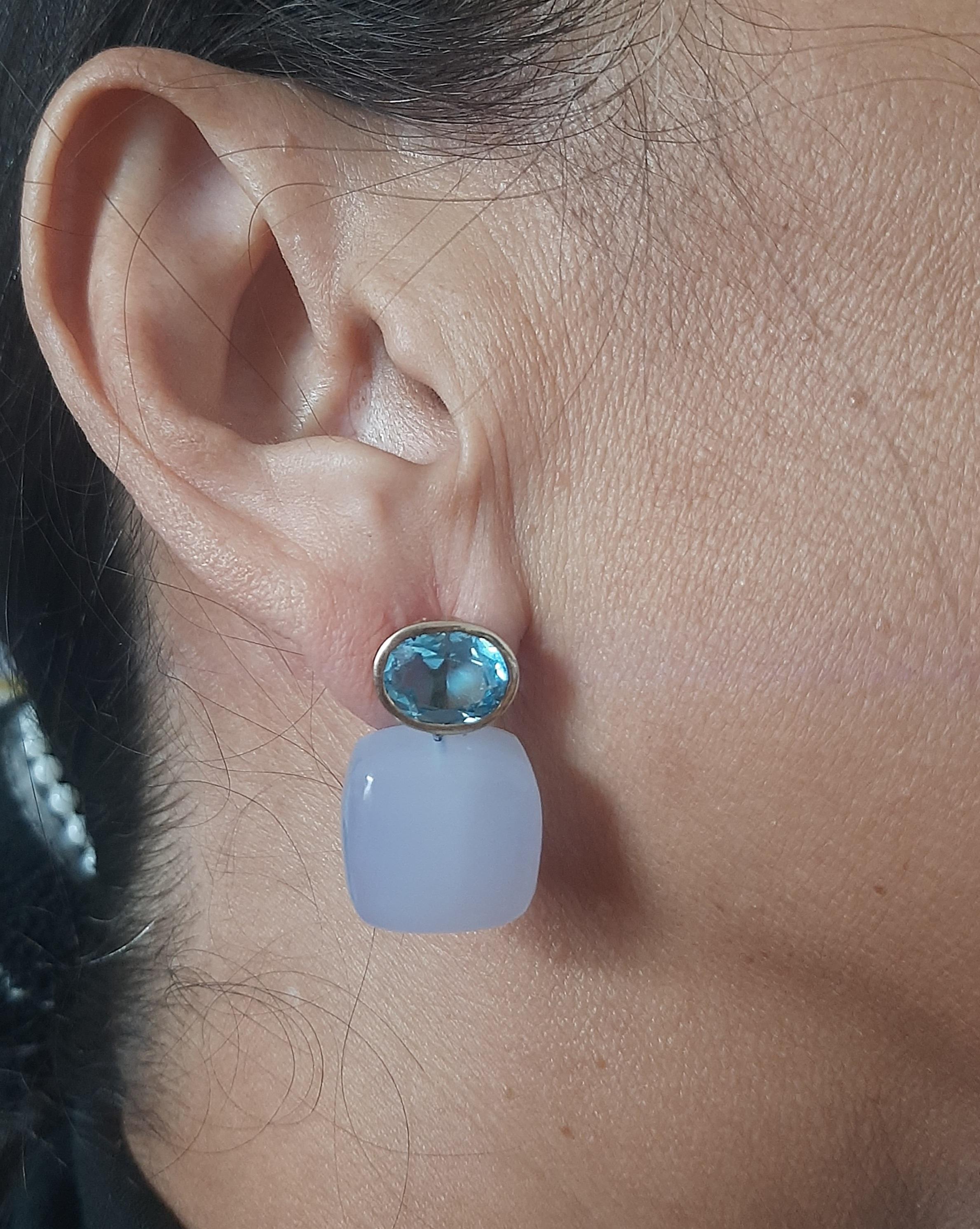 Diese einfachen, aber eleganten und handgefertigten Ohrringe bestehen aus 2 ovalen, facettierten Blautopasen mit den Maßen 8 x 10 mm, die in eine Lünette aus 14 Kt. Gelbgold eingefasst sind, an der 2 kissenförmige blaue Chalcedone mit den Maßen 15 x