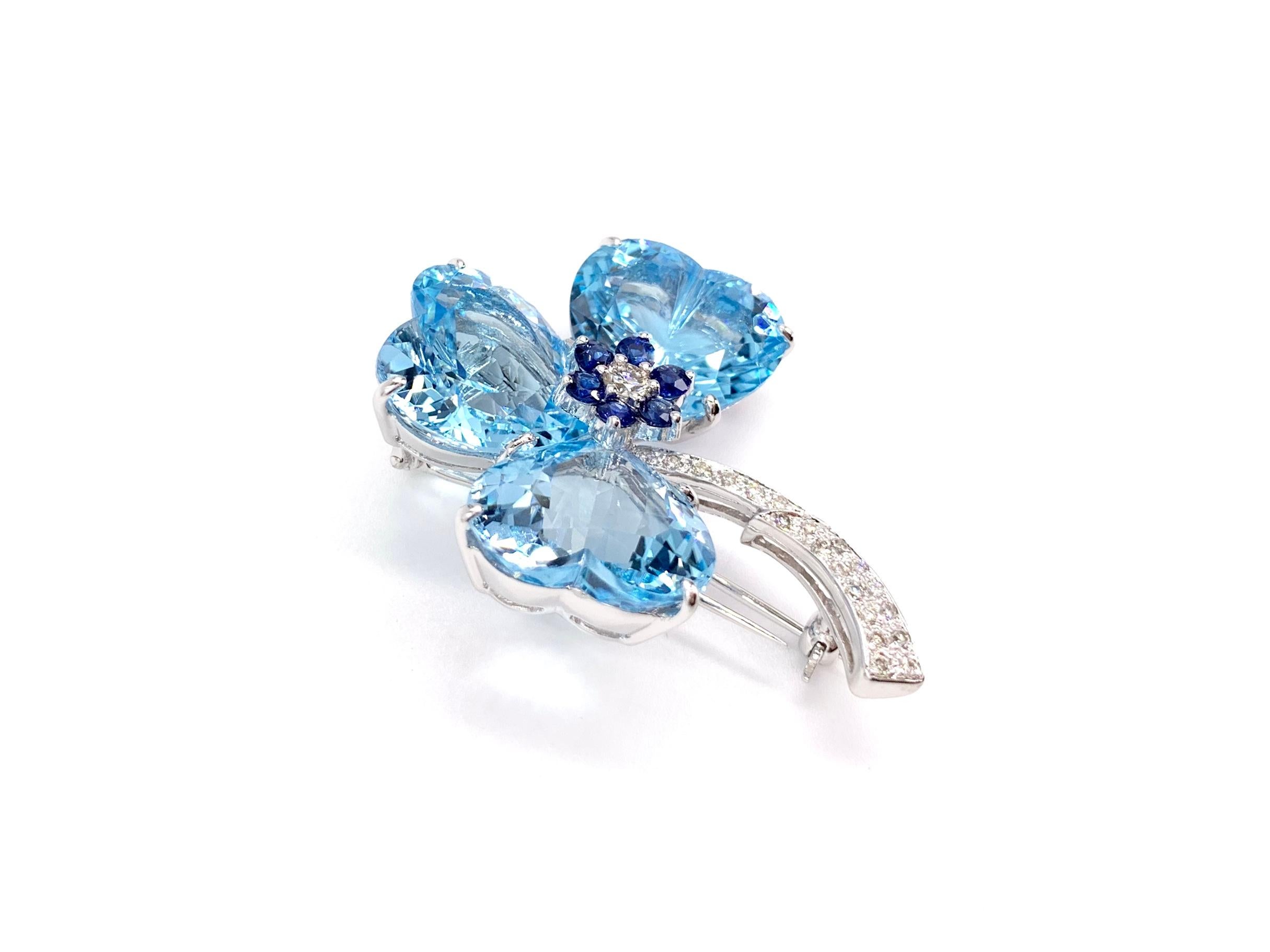 A truly stunning piece made with high quality gemstones. This 18 karat white gold clover pin features three heart shape blue topaz with a total weight of 37.34 carats, six blue sapphires at .44 carats total weight and twenty-one diamonds at .36
