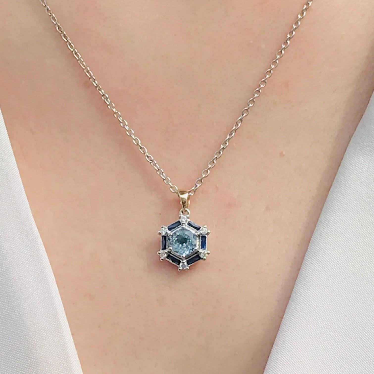 Al centro c'è un topazio blu rotondo che irradia una ricca e accattivante tonalità di blu. Il topazio è circondato da eleganti zaffiri blu taglio francese, che aggiungono profondità ed eleganza con i loro bordi geometrici. Il design è ulteriormente