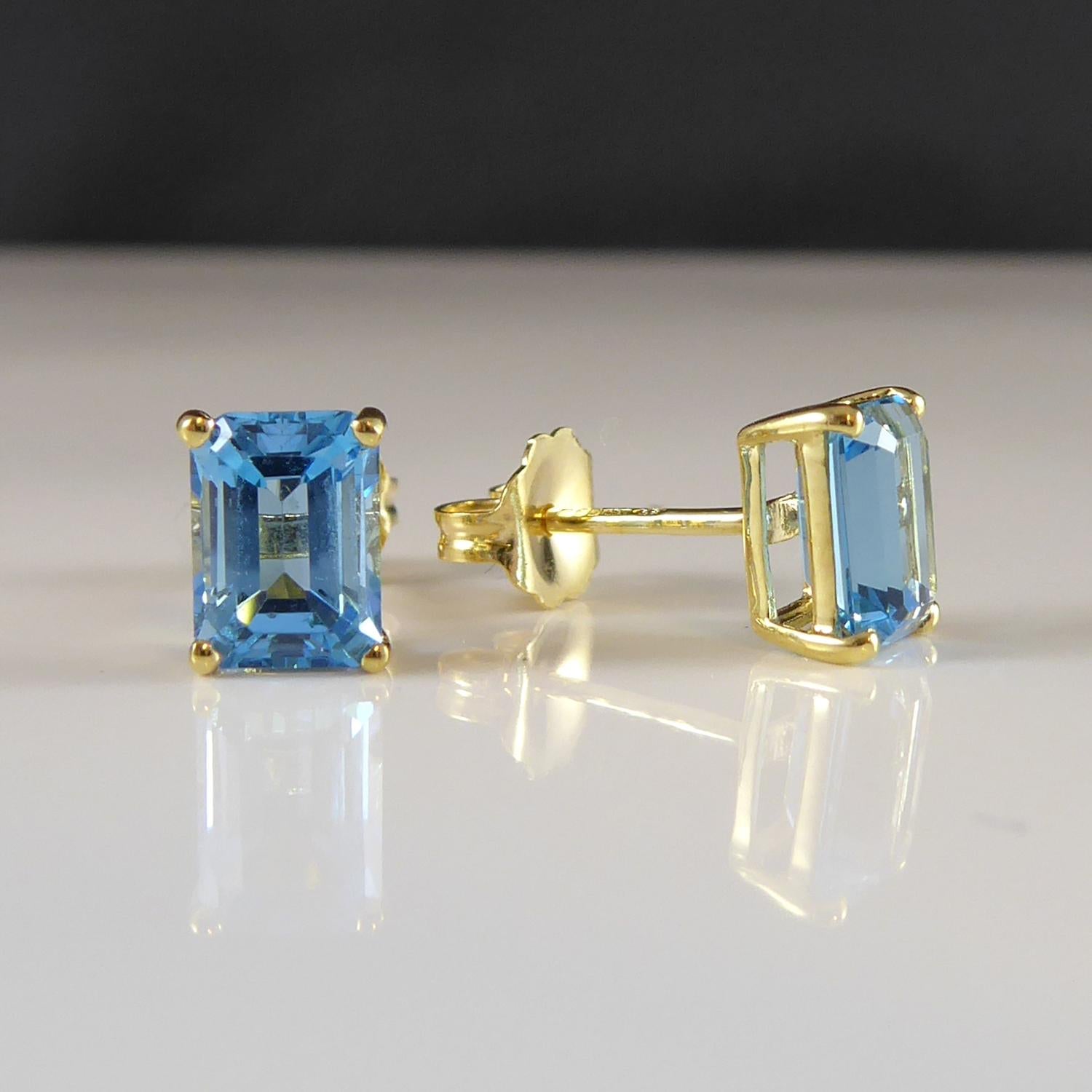 A simple and elegant paire of pre-owned blue topaz earrings.  Each earring is features an emerald cut blue topaz of vibrant colour and measuring approx. 7.00mm x 5.00mm.  Set in a four claw yellow mount with post and butterfly fittings for pierced