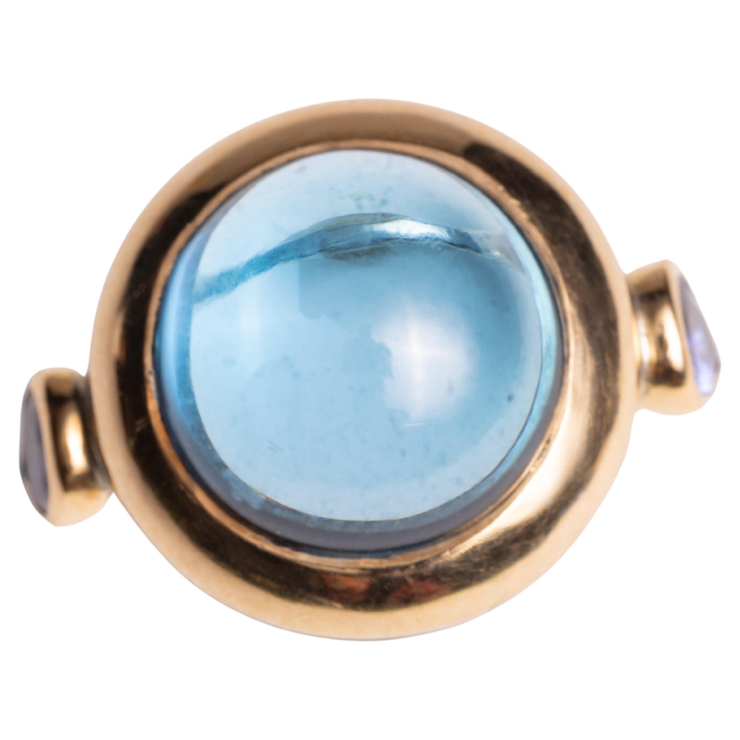 A large round cabochon blue topaz gemstone ring with two faceted, pear-shaped tanzanite stones on the side.  18K gold over sterling (not a plated gold).  Ring size is 7.25.

The fine jewelry collection is sourced, designed or created by Deborah
