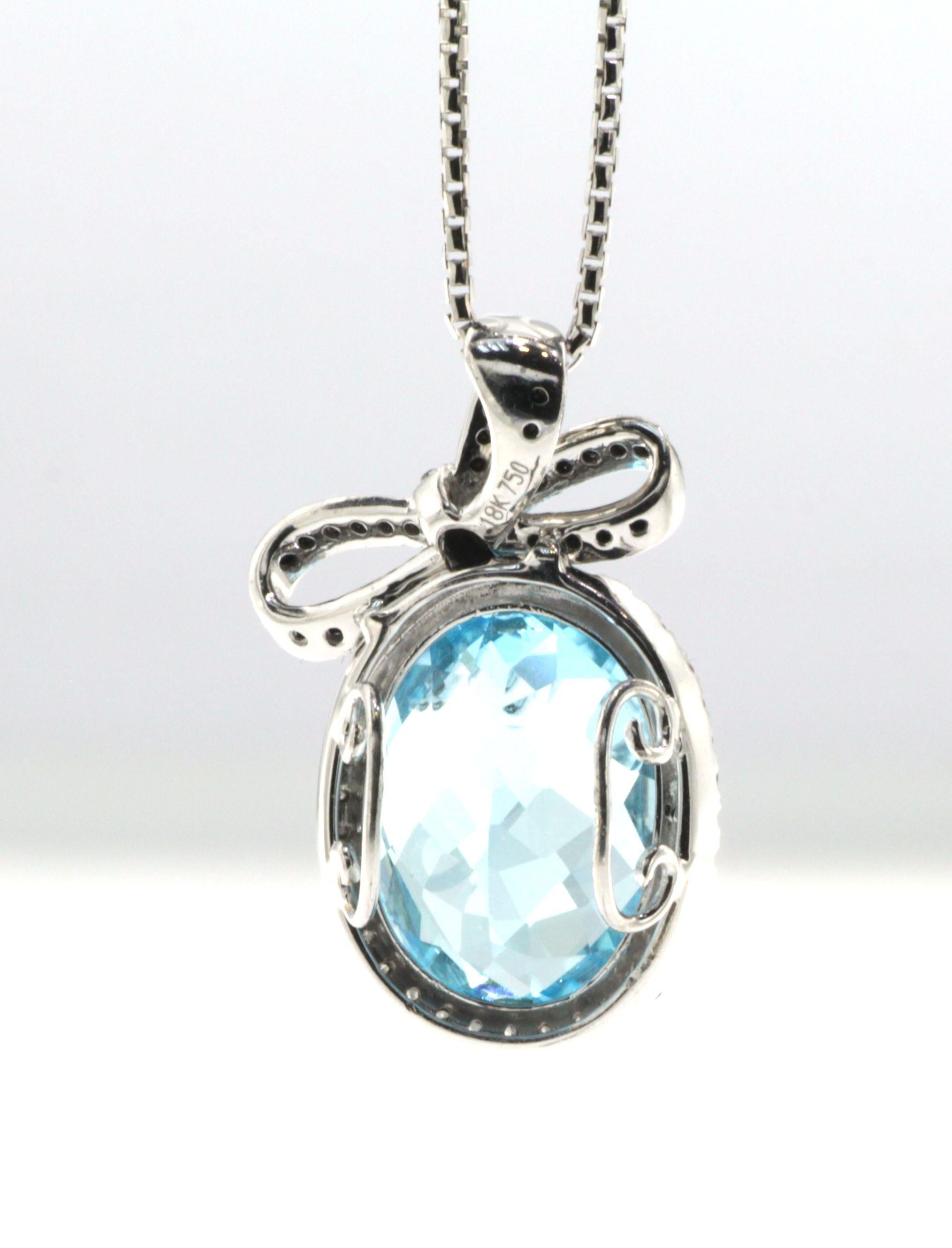 This pendant features a 10.63 carats faceted oval blue topaz, blue topaz is surrounded by 0.23 carat of white round diamond. Black diamonds are set in a ribbon on top of the blue topaz. Pendant is set in 18 karat white gold. Chain is not included.