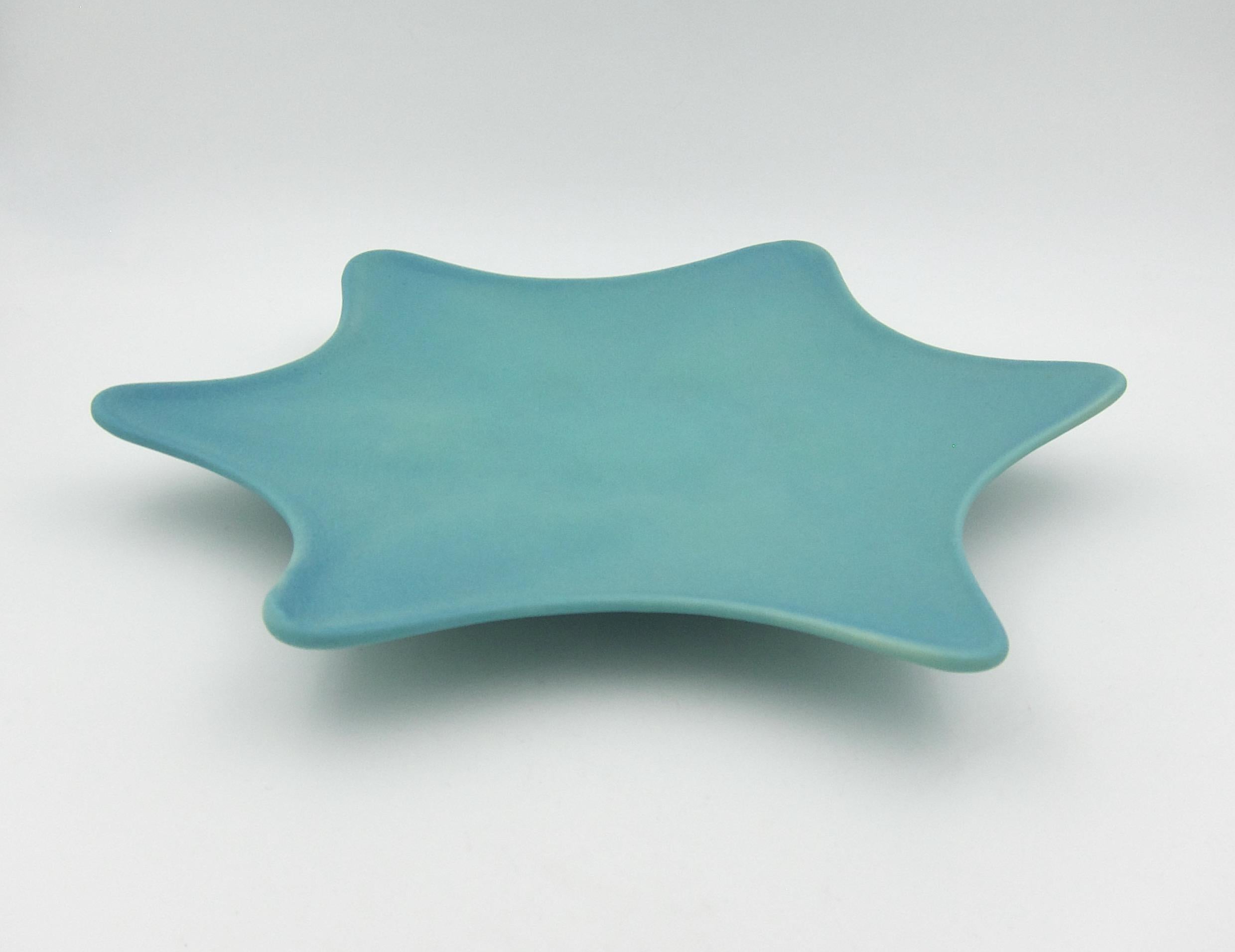 A vintage serving tray or platter from Van Briggle Pottery of Colorado Springs, dating circa 1970s. The vintage art pottery tray in a matte turquoise blue green glaze is shaped like a biomorphic six-pointed star, resting on a circular foot inscribed