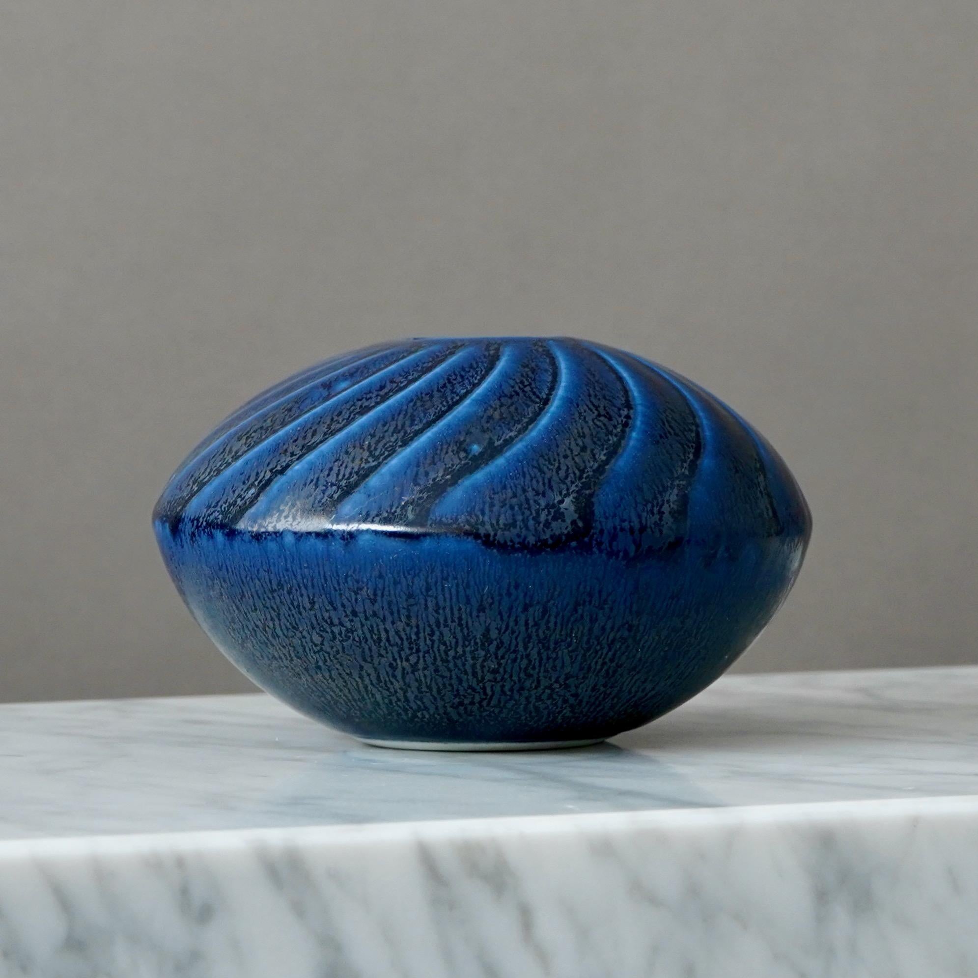 Un bellissimo vaso in gres con smalto blu.
Realizzato da Wilhelm Kåge presso lo Studio A di Gustavsberg in Svezia. In produzione dal 1958 al 1962.

Buone condizioni. Alcune macchie nello smalto e alcuni segni di metallo. 
Impresso il marchio del