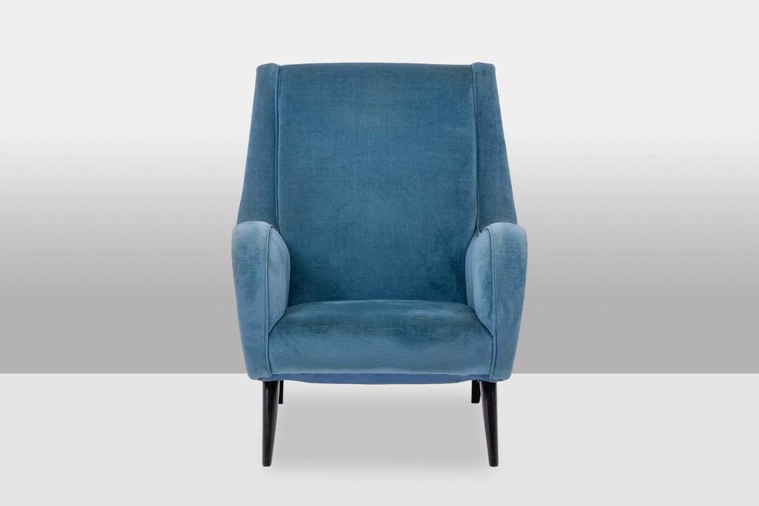 Fauteuil de salon en velours bleu composé d'un dossier légèrement incliné, encadré d'accotoirs à volutes débordantes, l'assise reposant sur 4 pieds fuselés en hêtre teinté disposés en compas.

Travail français réalisé dans les années