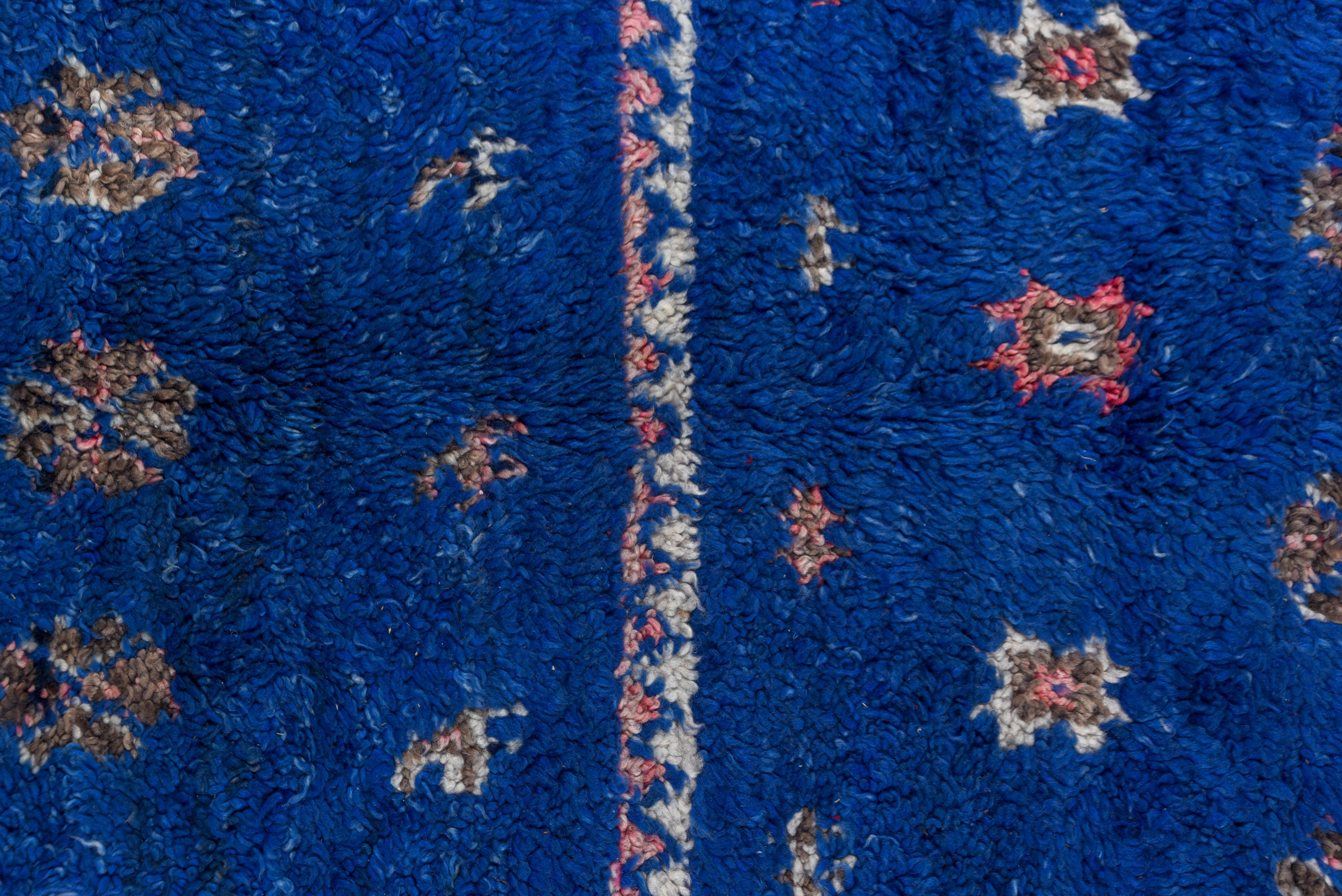 This Moroccan carpet has a shaggy radiant blue pile that's divided into four equal areas and displays small stars. Zig-zag strips separate the sections and border the piece and at one end are long blue tassels,.
 