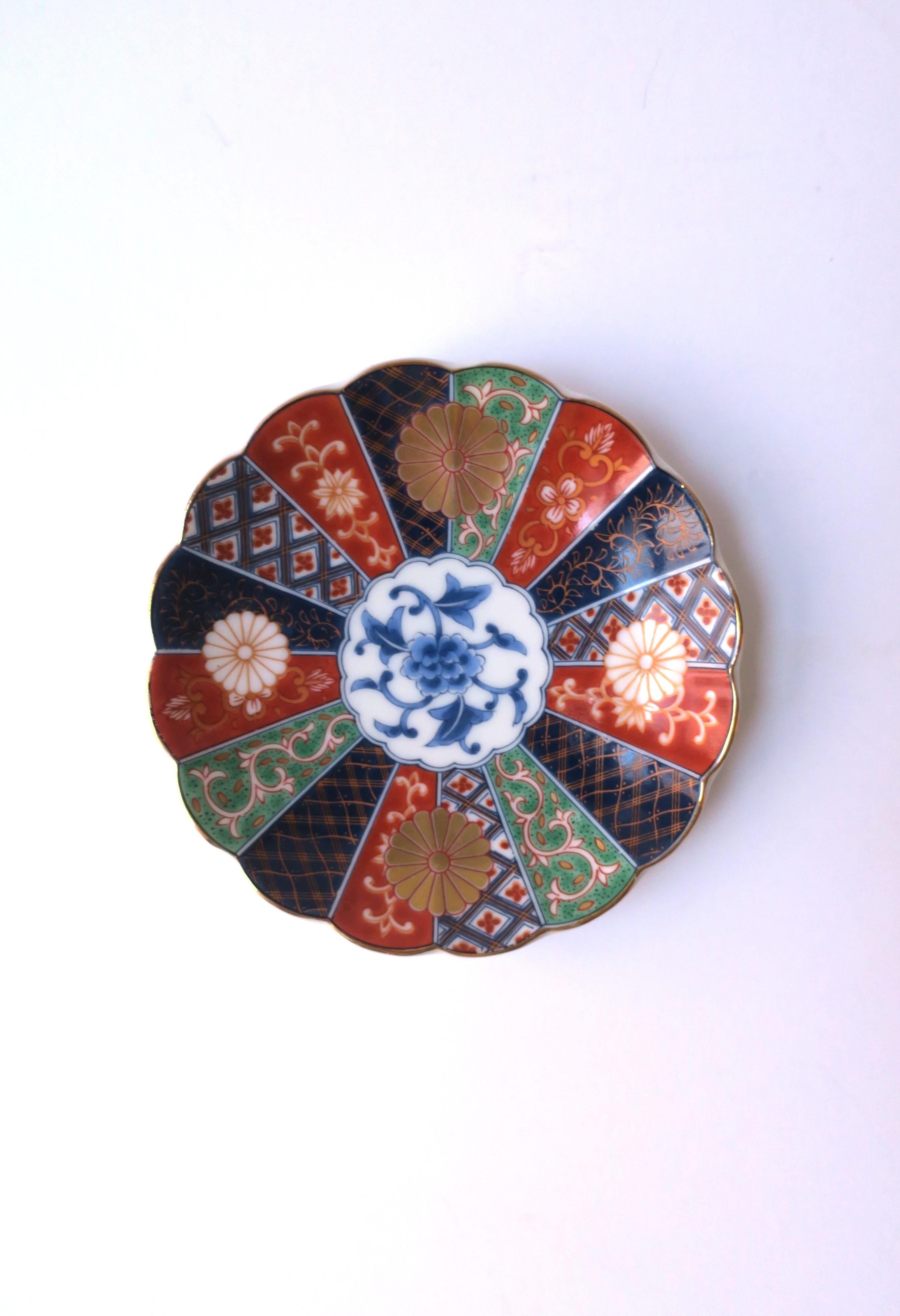 A beautiful round porcelain jewelry dish, hand-decorated, with a scalloped edge, in the Anglo-Japanese style, 1987, USA. Piece is made in both Japan and the United States. Colors include a white porcelain ground, blue, green, red burgundy, and gold.