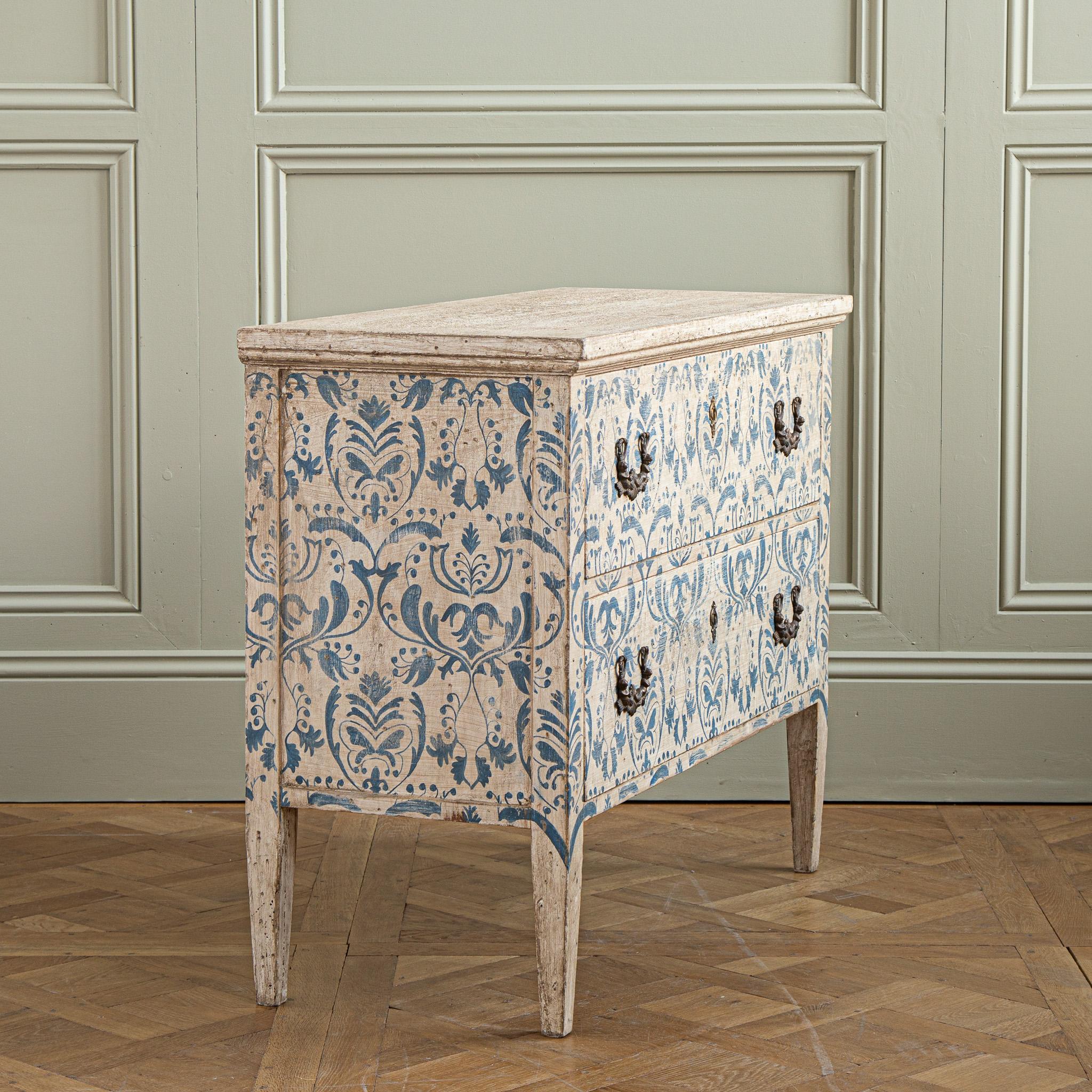 A vivid Italian Chest Of Drawers, hand painted in the traditional Florentine style featuring an aged Indigo Blue, flora and foliage motif on a background of antique white. The motif covers the front and both sides of the body to be viewed from all