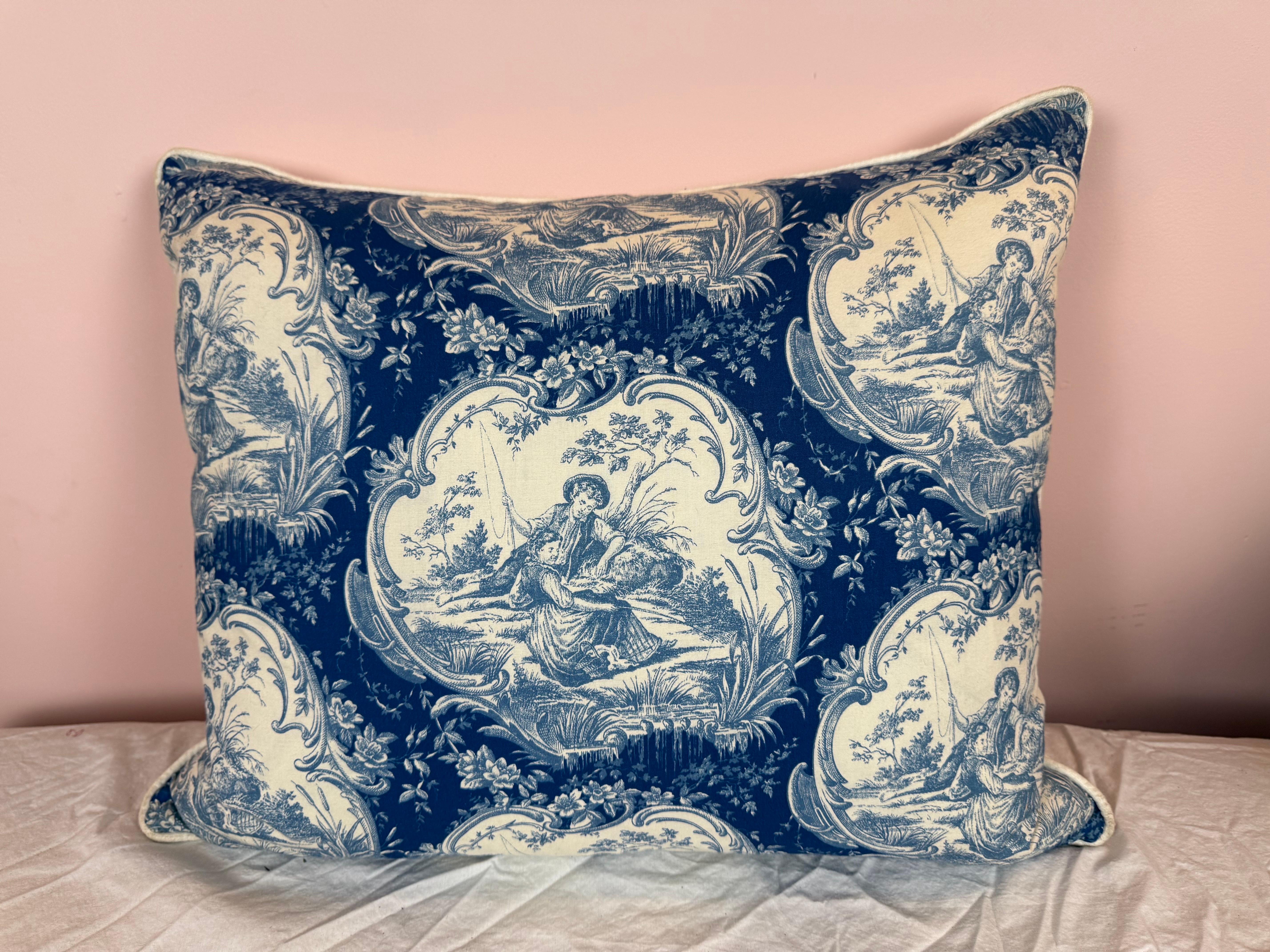 This charming decorative pillow features a classic toile pattern in navy blue and ivory linen. The design showcases idyllic pastoral scenes—figures in traditional dress engaged in leisurely outdoor activities—framed by ornate cartouches and