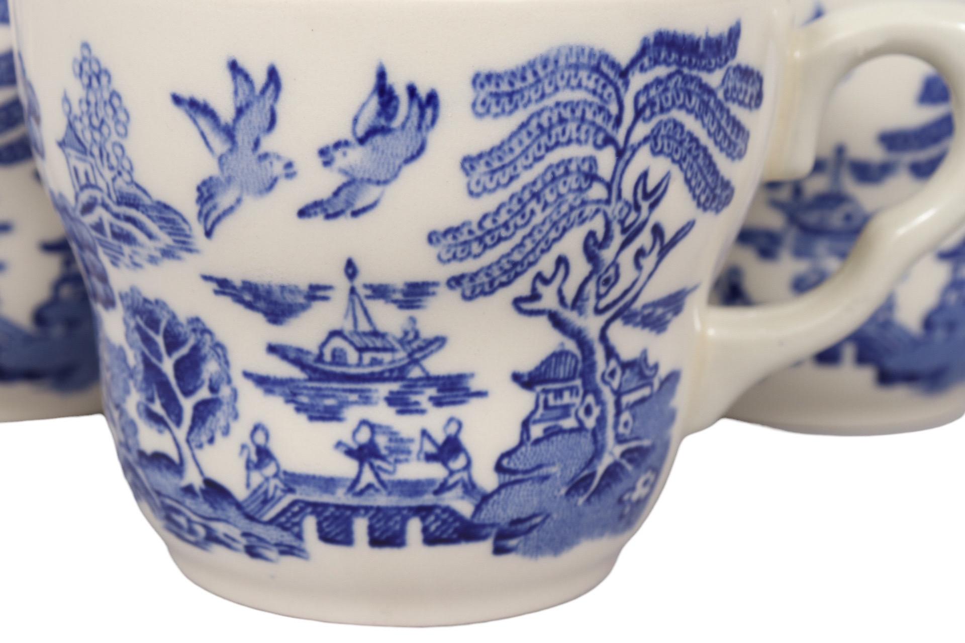 A set of eight blue and white transferware ceramic teacups, reminiscent of the Johnson Brothers Ironstone, made by English Ironstone Tableware Ltd of Staffordshire. Shapely cups with loop handles are decorated in the ‘Blue Willow’ pattern which