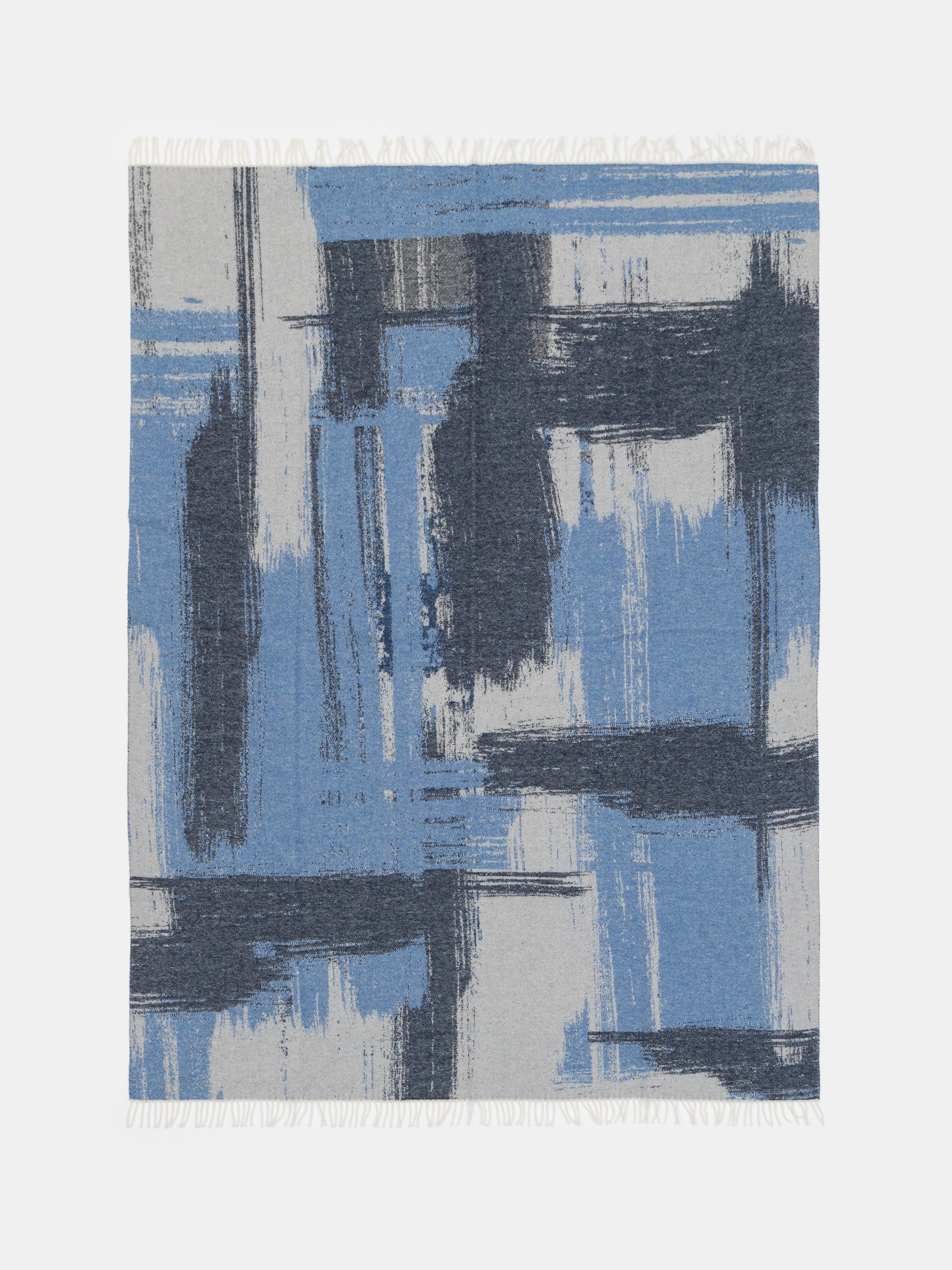 This elegant throw, crafted in Como, Italy, blends 85% wool and 15% cashmere for a beautifully soft, warm, and refined texture. The jacquard weave features an artistic brushstroke-inspired pattern in subtle shades of blue and grey, evoking the