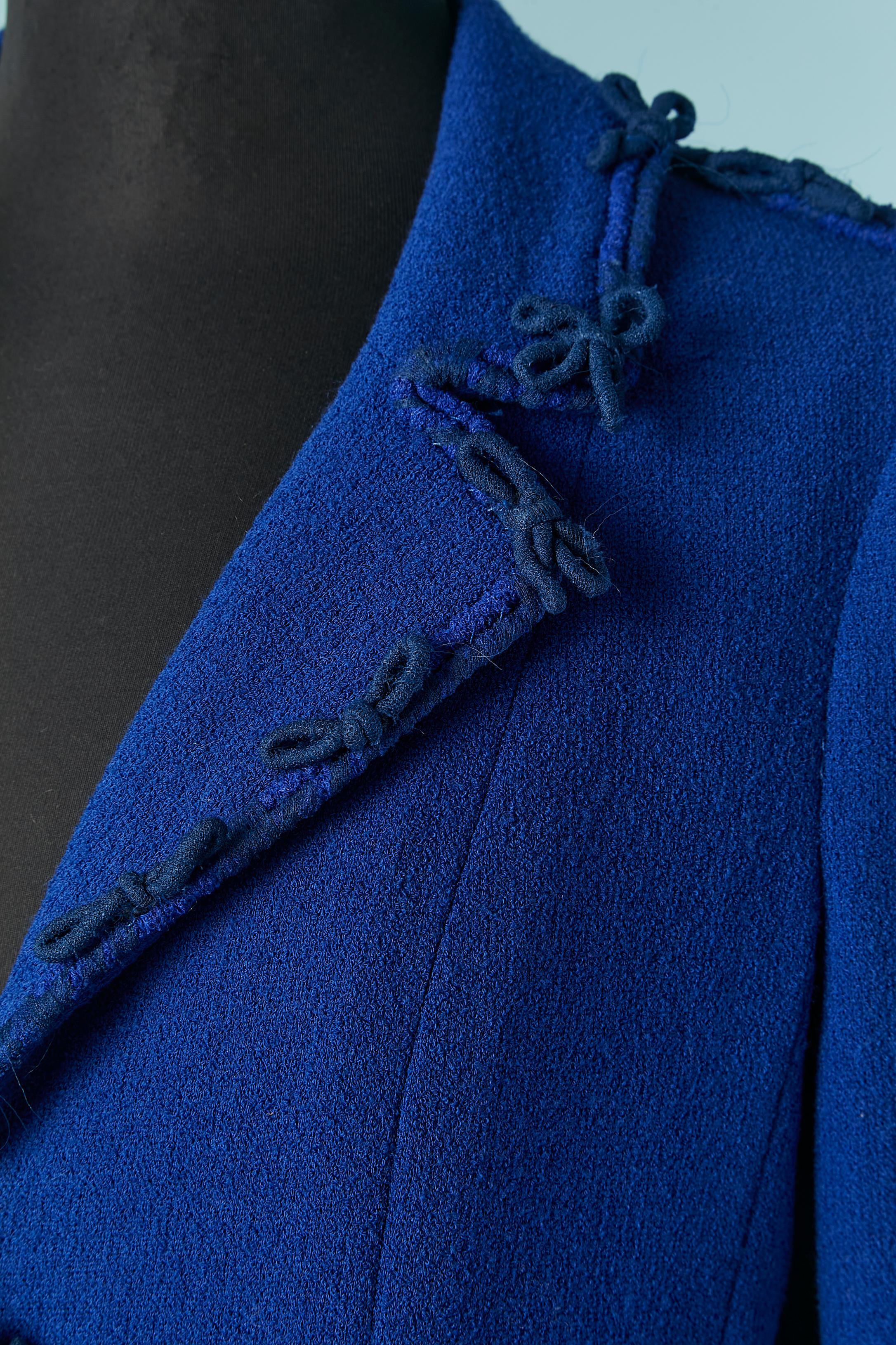 Giacca in lana blu con bordi e piccoli fiocchi. Composizione del tessuto del guscio: 84% lana, 16% poliammide. 
Fodera con marchio: 86% seta, 14% elastan.
Chiusura con gancio e occhiello al centro della parte anteriore.
Tasca su entrambi i lati.