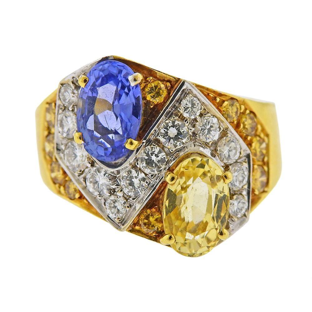 18k yellow gold ring, set with two oval sapphires - one blue (approx. 1.35ct)  and one yellow, (1.45ct), surrounded with yellow sapphires and approx. 0.85ctw in diamonds. Ring size 6, top is 16mm wide. Marked 750. Weighs 9.4 grams.