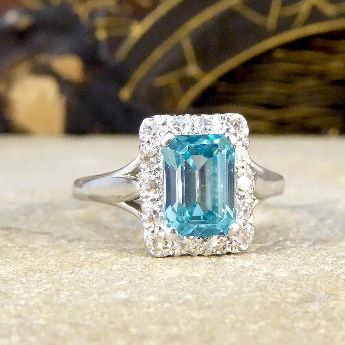 Featuring in this gorgeous vintage ring is an Emerald Cut Blue Zircon in the centre showing a bright and beautiful blue colour in a four claw setting allowing lots of light to pass through the stone and sparkle thoroughly. Surrounding the Zircon are