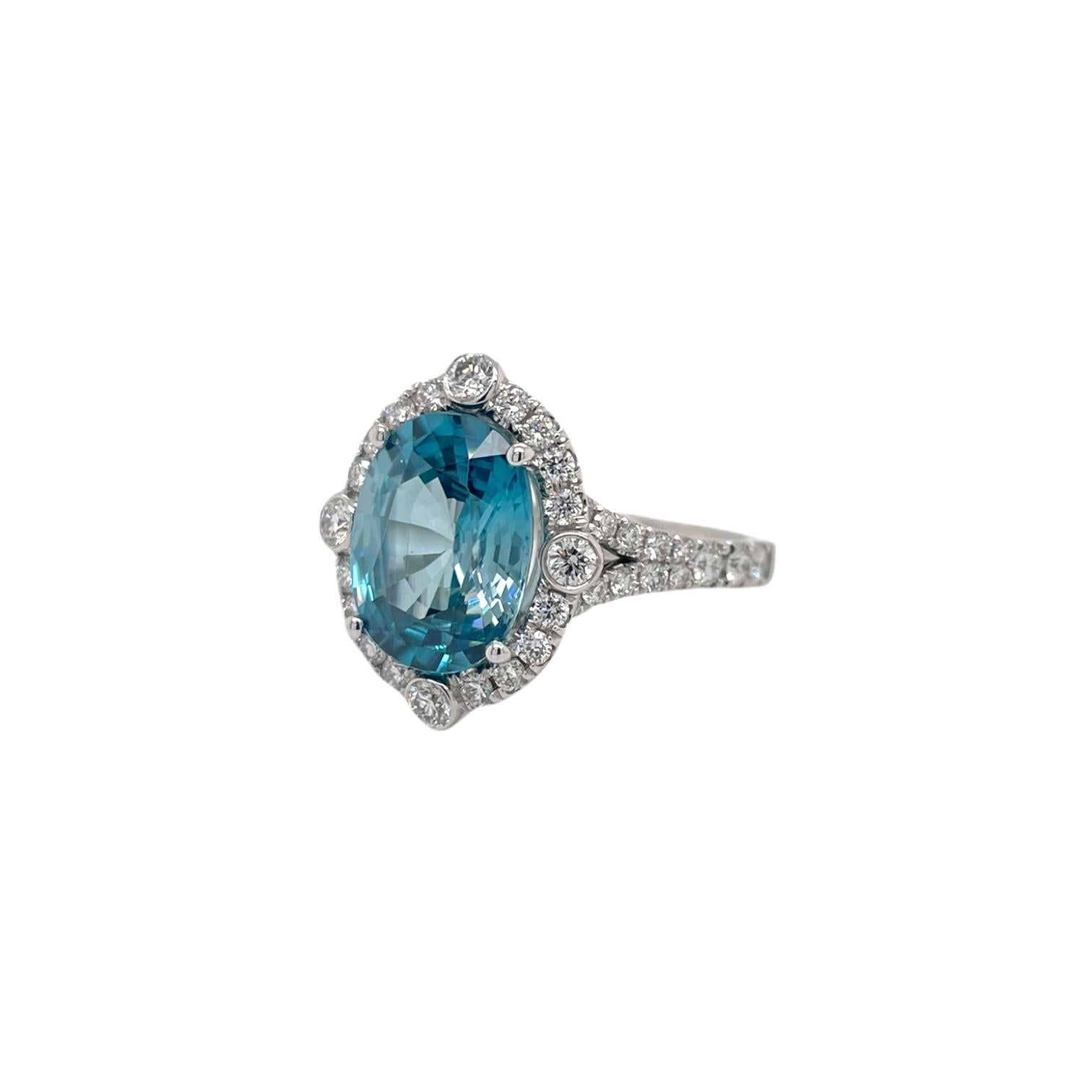 Ring contains 1 oval blue zircon weighing 5.78ct. Center stone is surrounded by a halo of round brilliant diamonds and diamonds going down the band, 0.90tcw. Diamonds are near colorless and SI1 in clarity, excellent cut. All stones are mounted in a