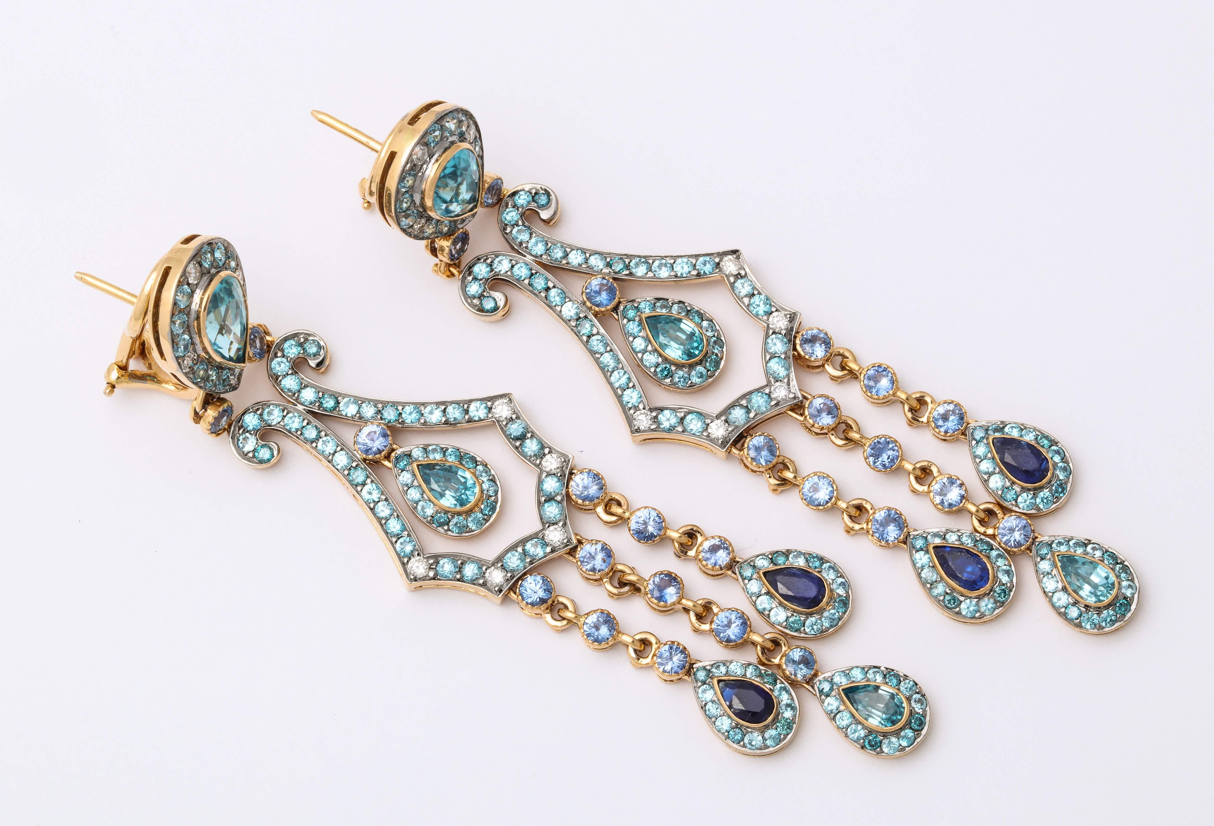 Festive and flirty 18 Karat yellow gold chandelier earrings mounted with inverted pear shape (and drop shape) blue zircon: 14.42 carats, with an articulating outer fringe of pear shape sapphires: 3.32 carats, decorated with a mix of round