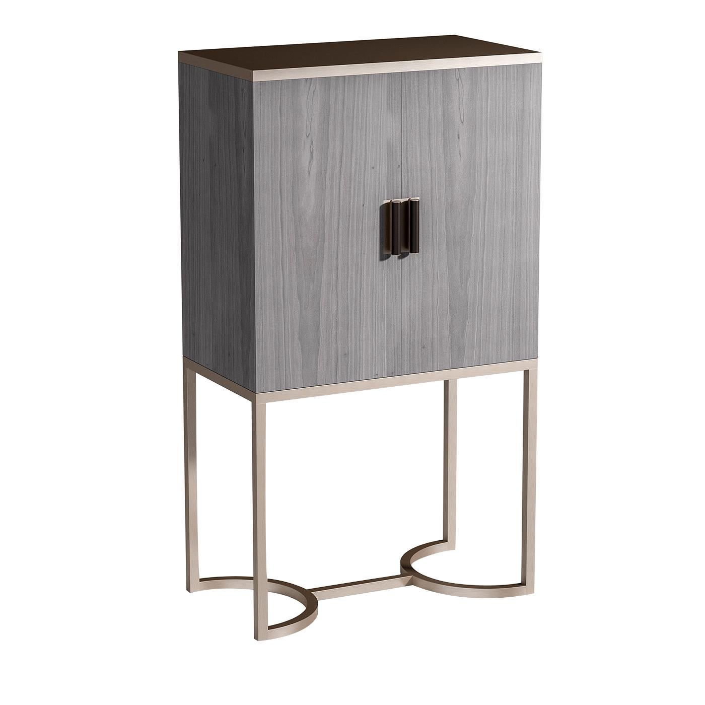 A Classic design with a modern touch, this sophisticated bar cabinet is characterized by a sleek Silhouette and bold architectural metal legs with two semicircles connected by a central bar. The square gray veneered wood cabinet has two doors with