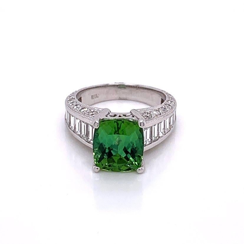 A sexy ring featuring a green tourmaline with a secondary blue color to it. It weighs 4.10 carats as a cushion shaped gem. It is accented by a total of 2.10 carats of diamonds; round cuts set on the inside of the ring and emerald cuts in graduating