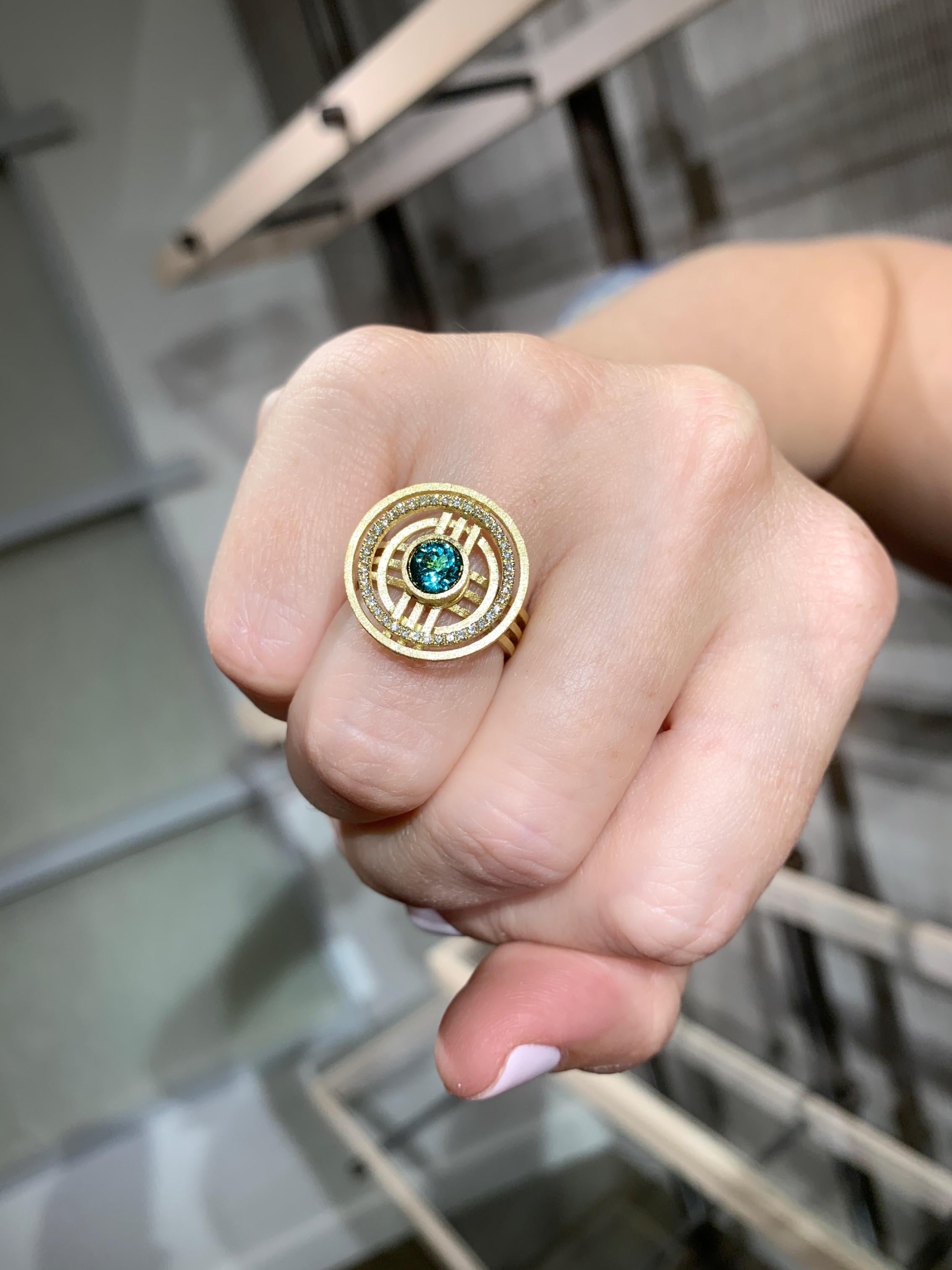 Super Solar Ring magnificently hand-fabricated in London in intricately textured 18k yellow gold by jewellery maker Shimell and Madden, showcasing a vivid greenish blue 5.5mm round brilliant-cut indicolite tourmaline surrounded with 0.20 total