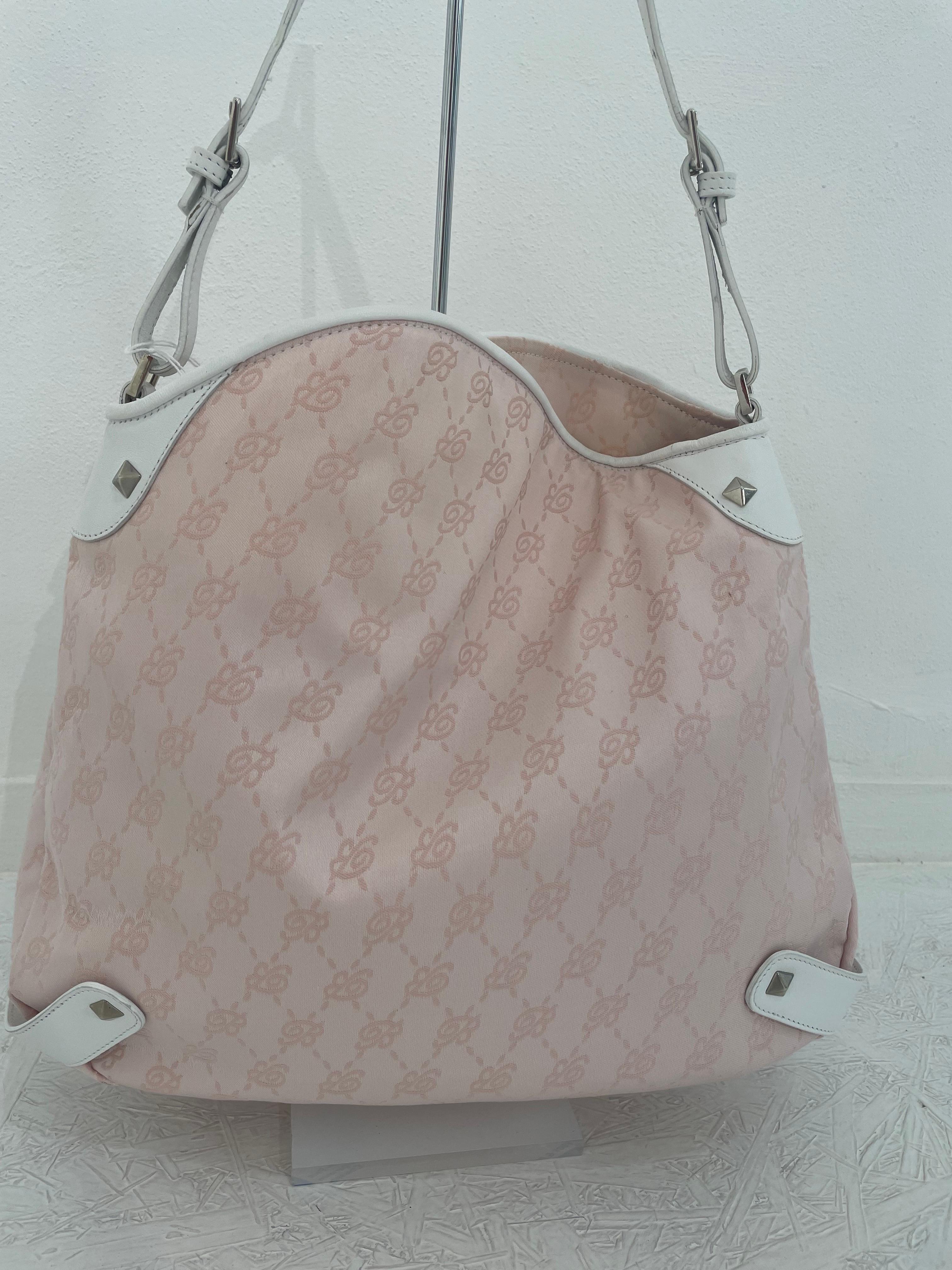 Borsa Blumarine in tessuto rosa con logo ricamato, dettagli in pelle bianca con piccole borchie d'argento. Spaziosa con tasche interne laterali, una delle quali chiusa da una zip. Chiusura con bottone magnetico. 
Tracolla regolabile. Sebbene non sia