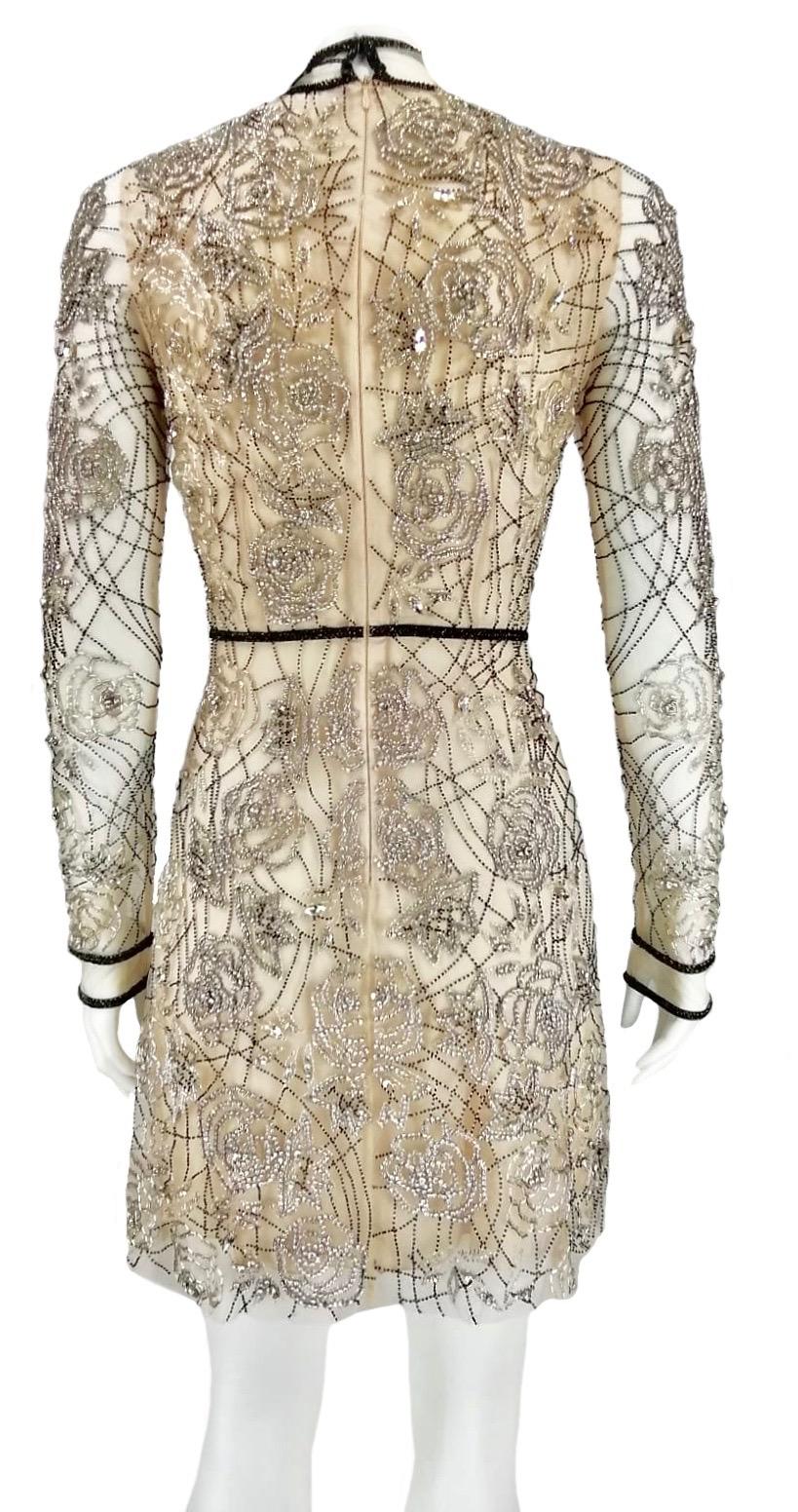 Blumarine tulle dress embroidered entirely by hand, with beads and crystals in an intertwined design of camellias, leaf shoots and ramages. Transparent with champagne silk lining. Details with black beads. Long sleeves, mandarin collar, back