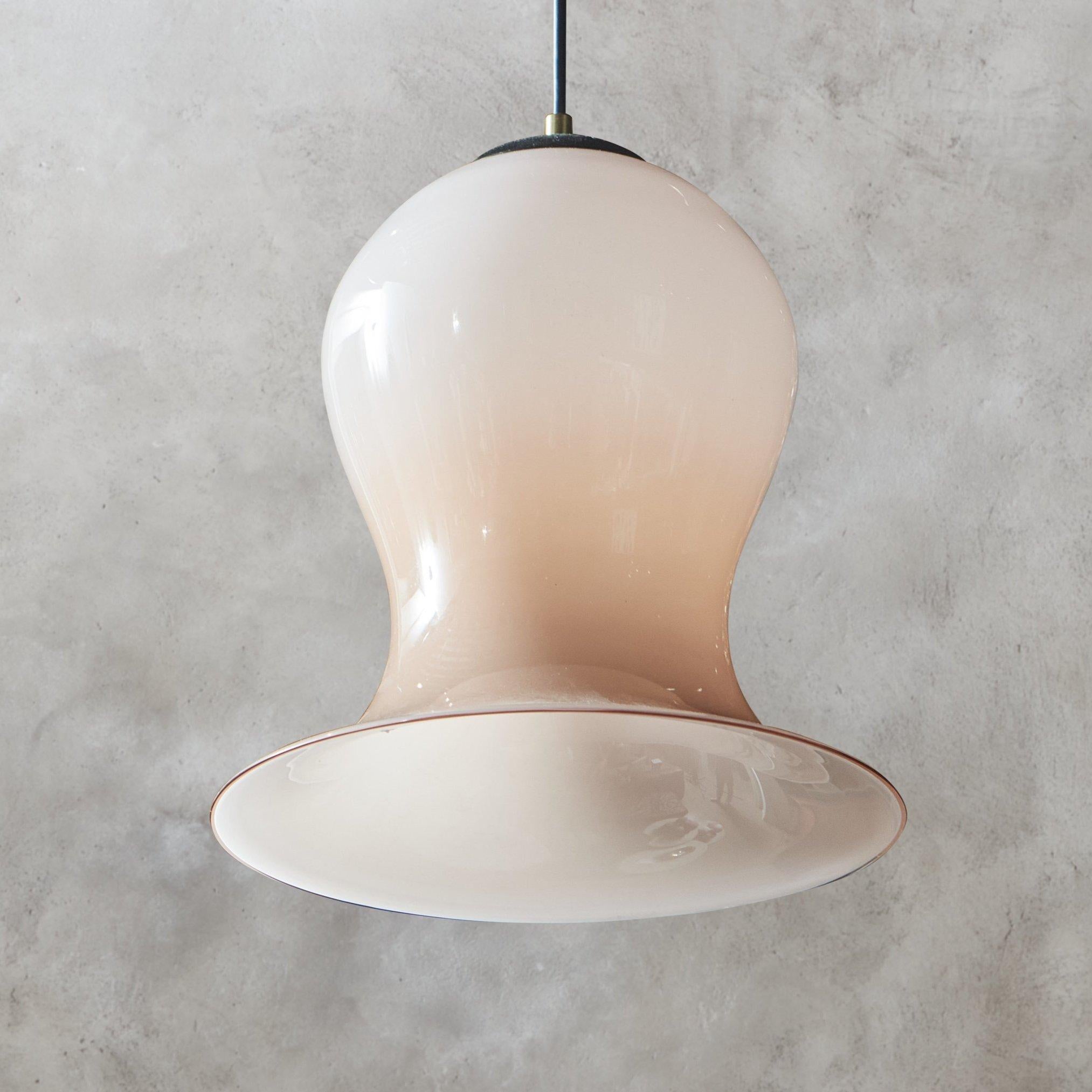 A Mid Century pendant light featuring a bell-shaped hand blown Murano glass shade in a gorgeous blush pink hue with a subtle red bottom trim. This fixture has black metal socket cover and hangs from a black cord with a new black metal canopy.