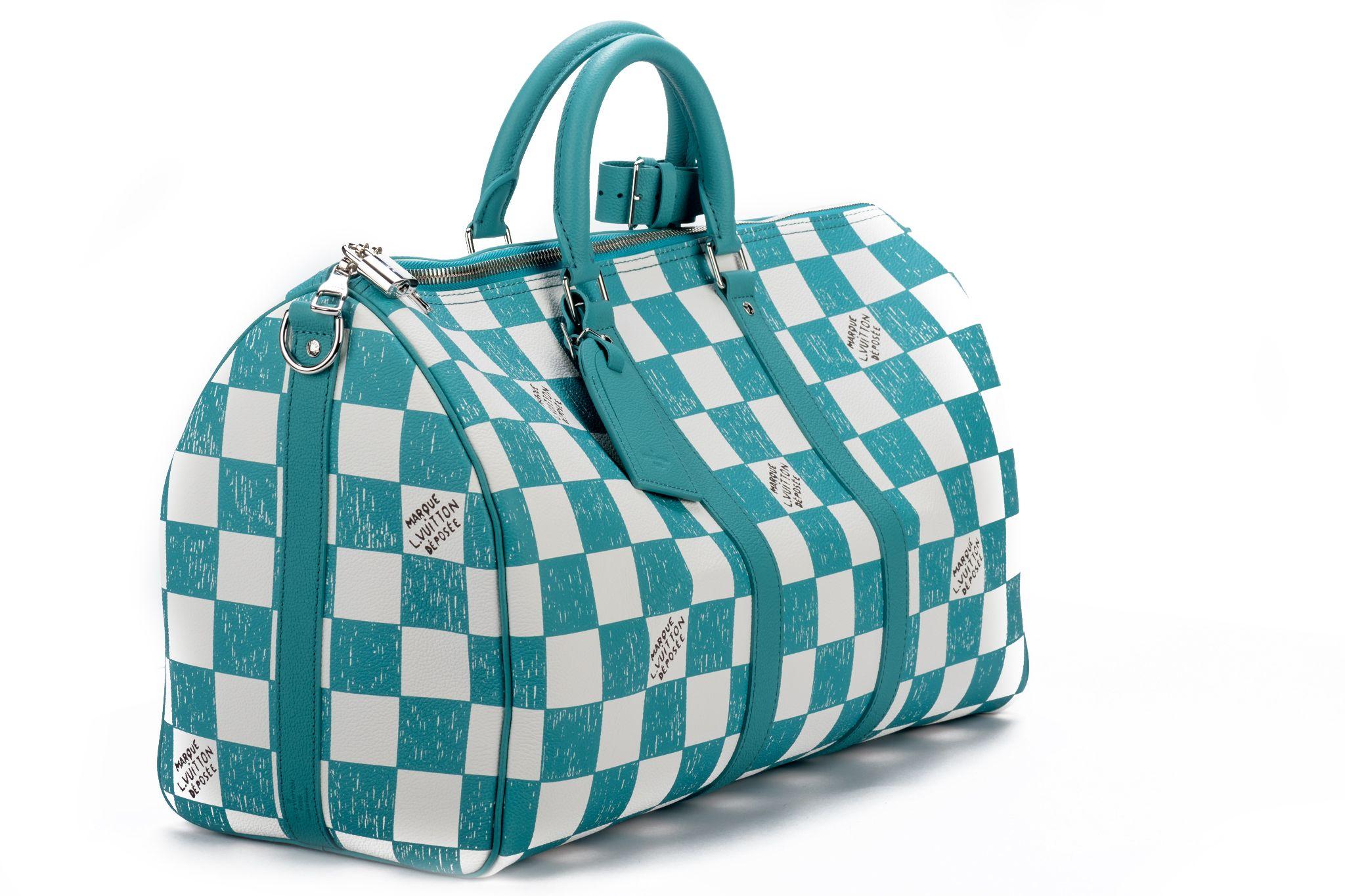 This Keepall Bandoulière 45 bag is fashioned from leather with a Damier checkerboard pattern in teal and white. The leather top handles, side bands, and nametag are also in teal. The squares look as if they were drawn and filled in with a colored