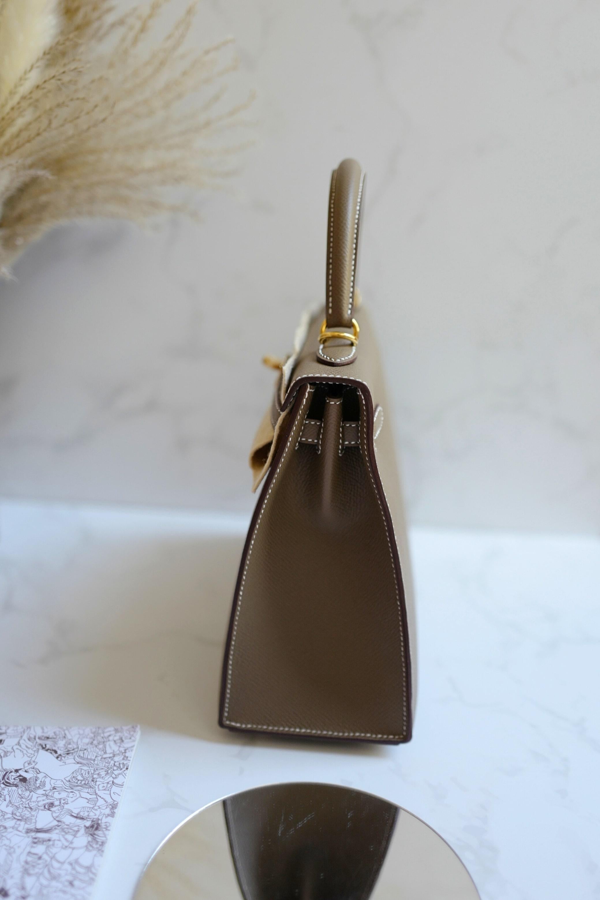 La Kelly 25 Sellier di Hermès in pelle Etoupe Epsom è ammirata per il suo design strutturato e la sua versatile tonalità neutra. Il colore Etoupe si abbina magnificamente a molti abiti, rendendolo adatto sia all'uso quotidiano che a contesti più