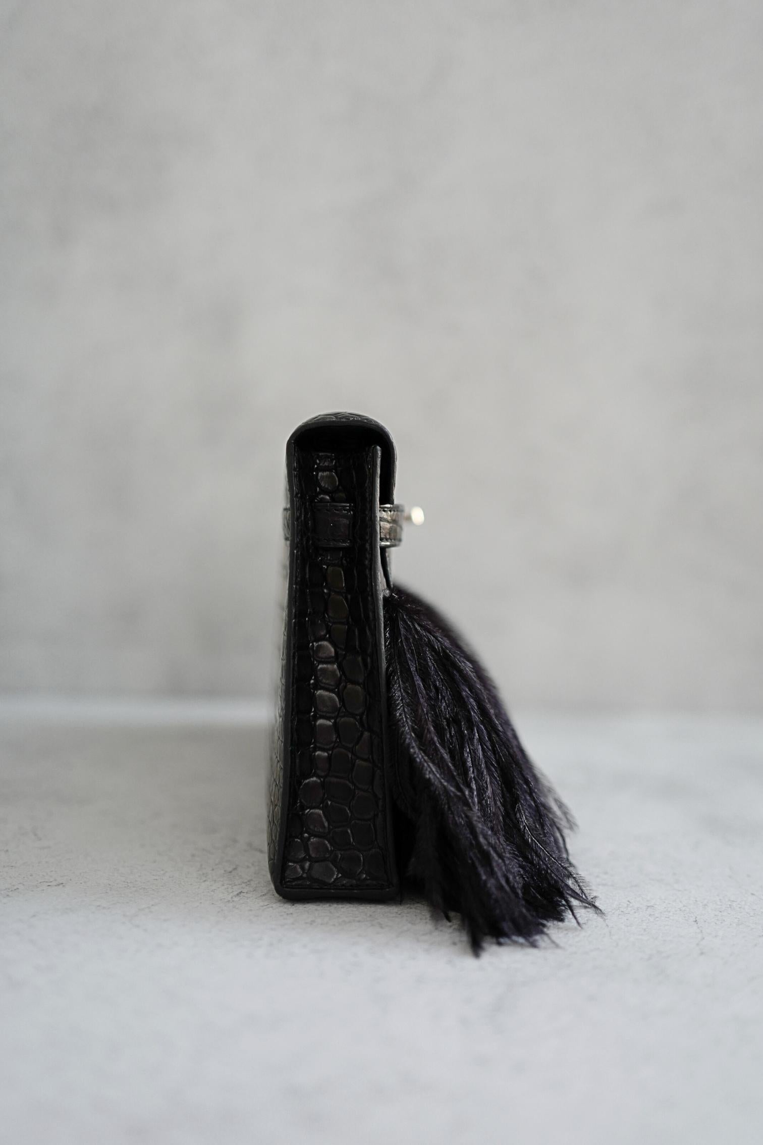 Elevate your collection with this exceptional Hermès Kelly Elan Folie in Noir, crafted from exquisite matte Porosus crocodile leather and accented with dramatic ostrich feather detailing. The elongated silhouette offers a sleek, modern