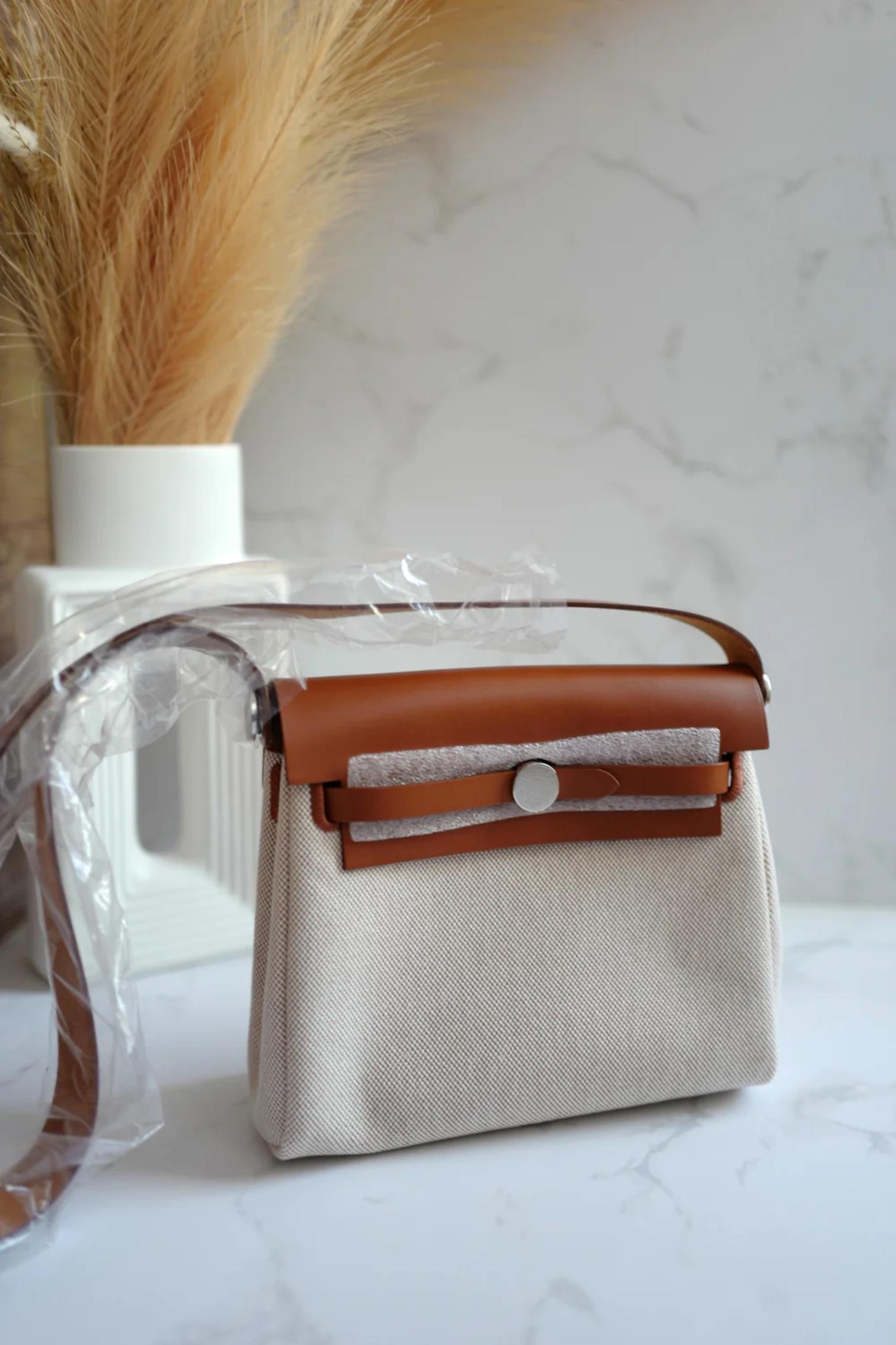 Discover the perfect harmony of timeless elegance and everyday practicality with the Hermès Mini Herbag in Fauve and Ecru. This exquisite piece combines supple Fauve leather accents with a soft, natural Ecru canvas body, creating a sophisticated yet