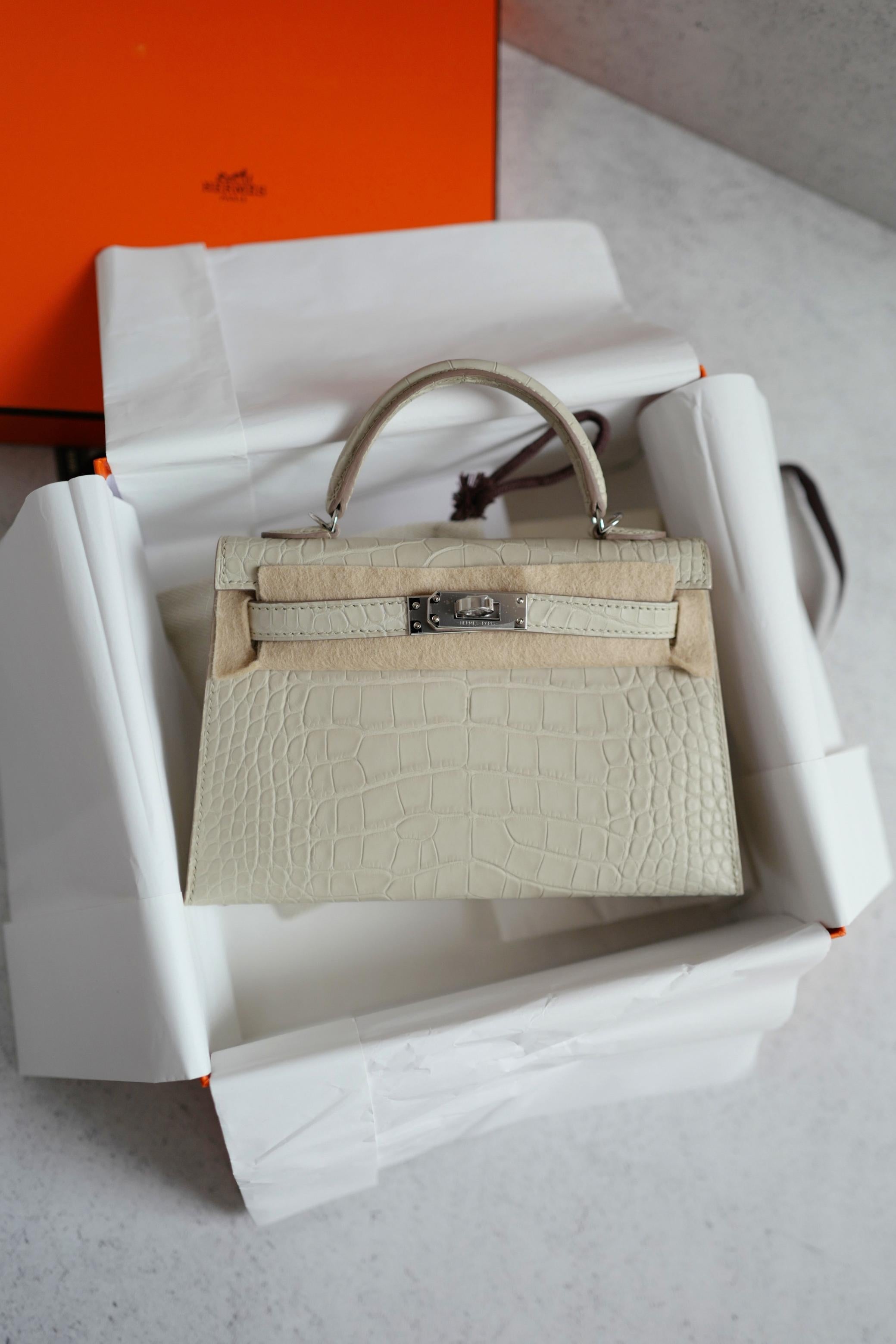 The Hermès Mini Kelly 20 in Beton Matte Crocodile with Palladium Hardware is the epitome of understated luxury. Its delicate Beton shade, a refined ivory tone, enhances the soft matte finish of the exotic crocodile leather, bringing out the
