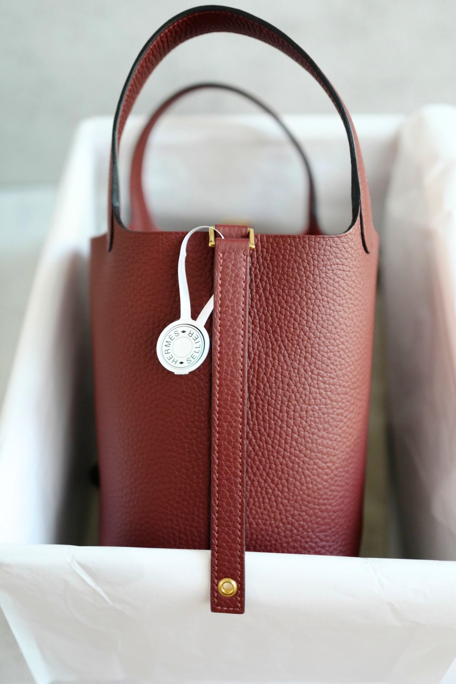 The Hermès Picotin Lock 18 in Rouge H is a timeless handbag that embodies understated elegance and everyday practicality. Crafted from supple Taurillon Clemence leather, it features a soft grain texture that is both durable and luxurious. The deep