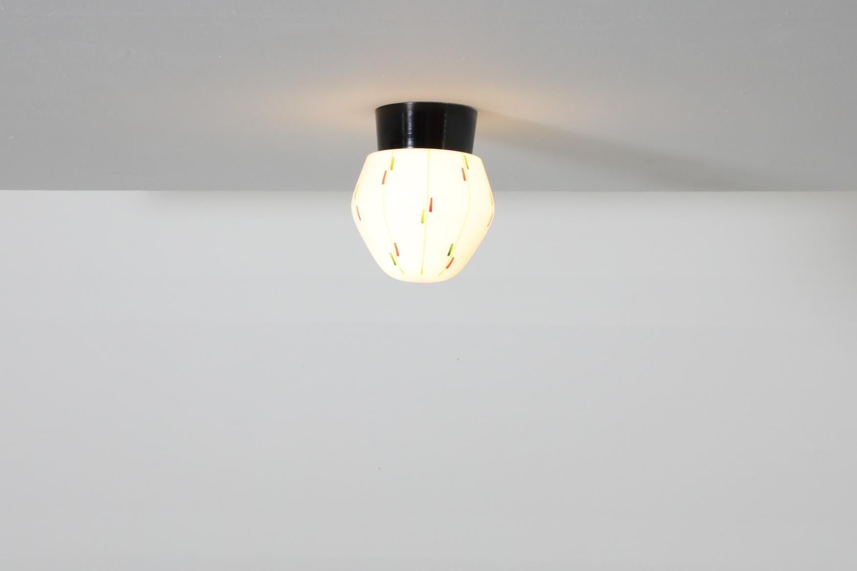 Lampada da soffitto o da parete belga di metà secolo, anni '60, con base in bachelite e paralume in vetro lattiginoso con stampa a motivi colorati. In condizioni originali, con un'usura coerente con l'età e l'uso. Sono disponibili altre luci simili,