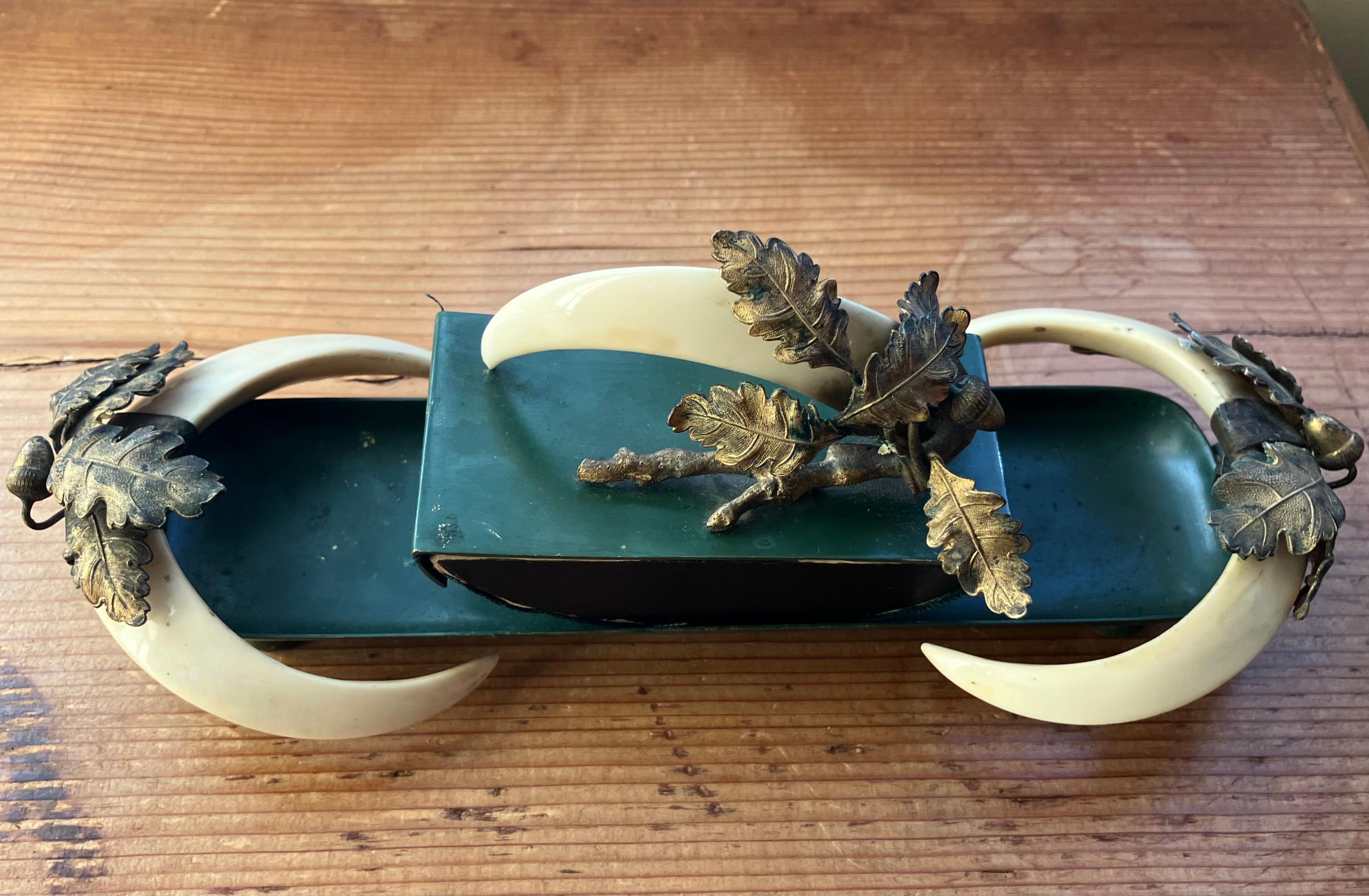 Boar Tusk Oak Leaf and Acorn Desk Blotter.  Boar tusk handled velvet blotter with gilt metal oak leaf branches and acorns framing green metal on ball feet. United States, early 20th century
Dimensions: 9 1/4
