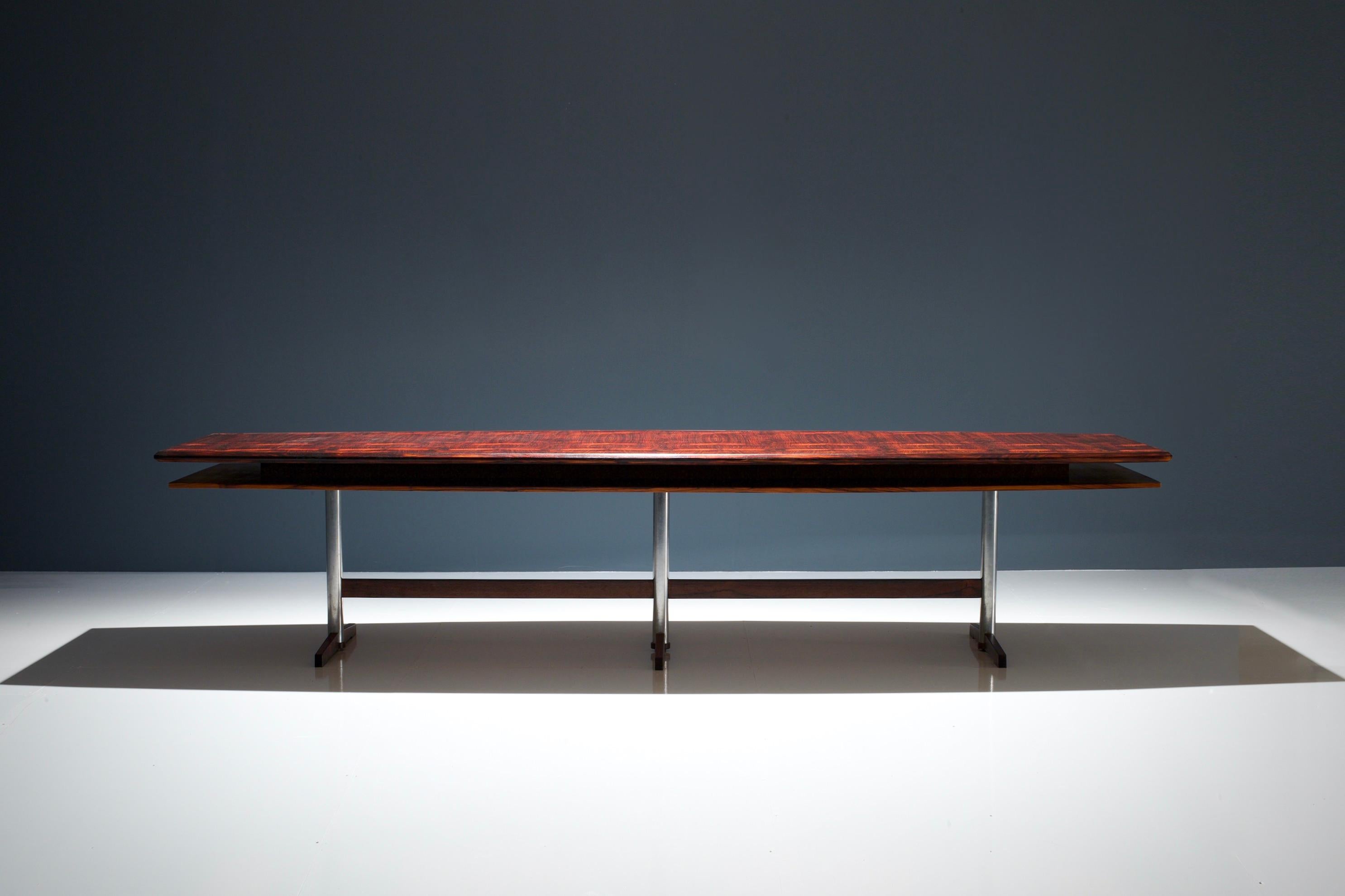 Scandinavian Modern conference- or dining table in rosewood and metal. The table is characterized by a large boat shaped rosewood tabletop with a rhythmic pattern of repeated dark flames that works very well with the red tinted Brazilian rosewood.