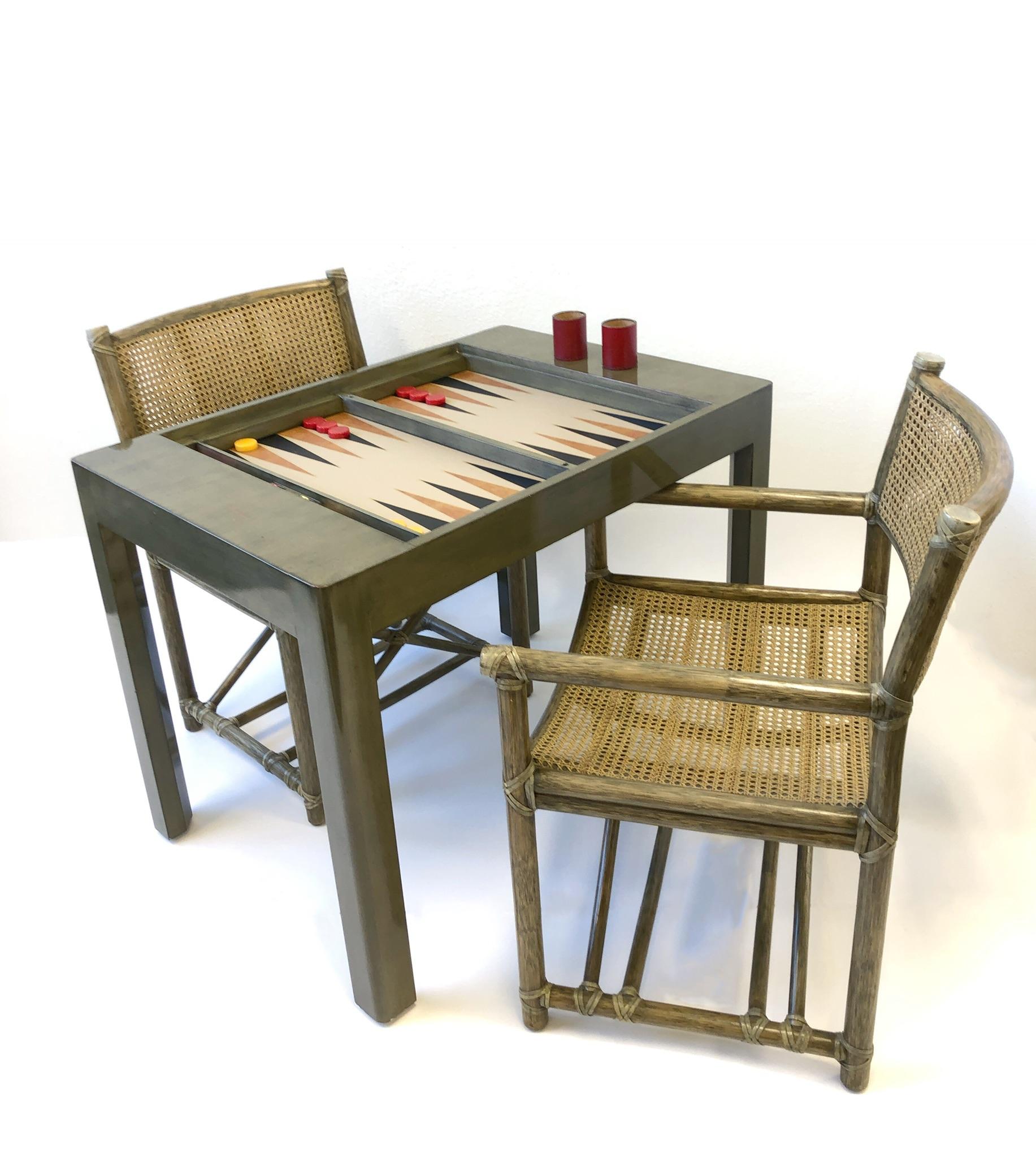 A spectacular backgammon game table set out of Bob and Dolores Hopes home. The table is by Steve Chase. The table has a inset top so you can play cards or other games on it. The pair of cane arm chairs are by McGuire. The table was used, so it has
