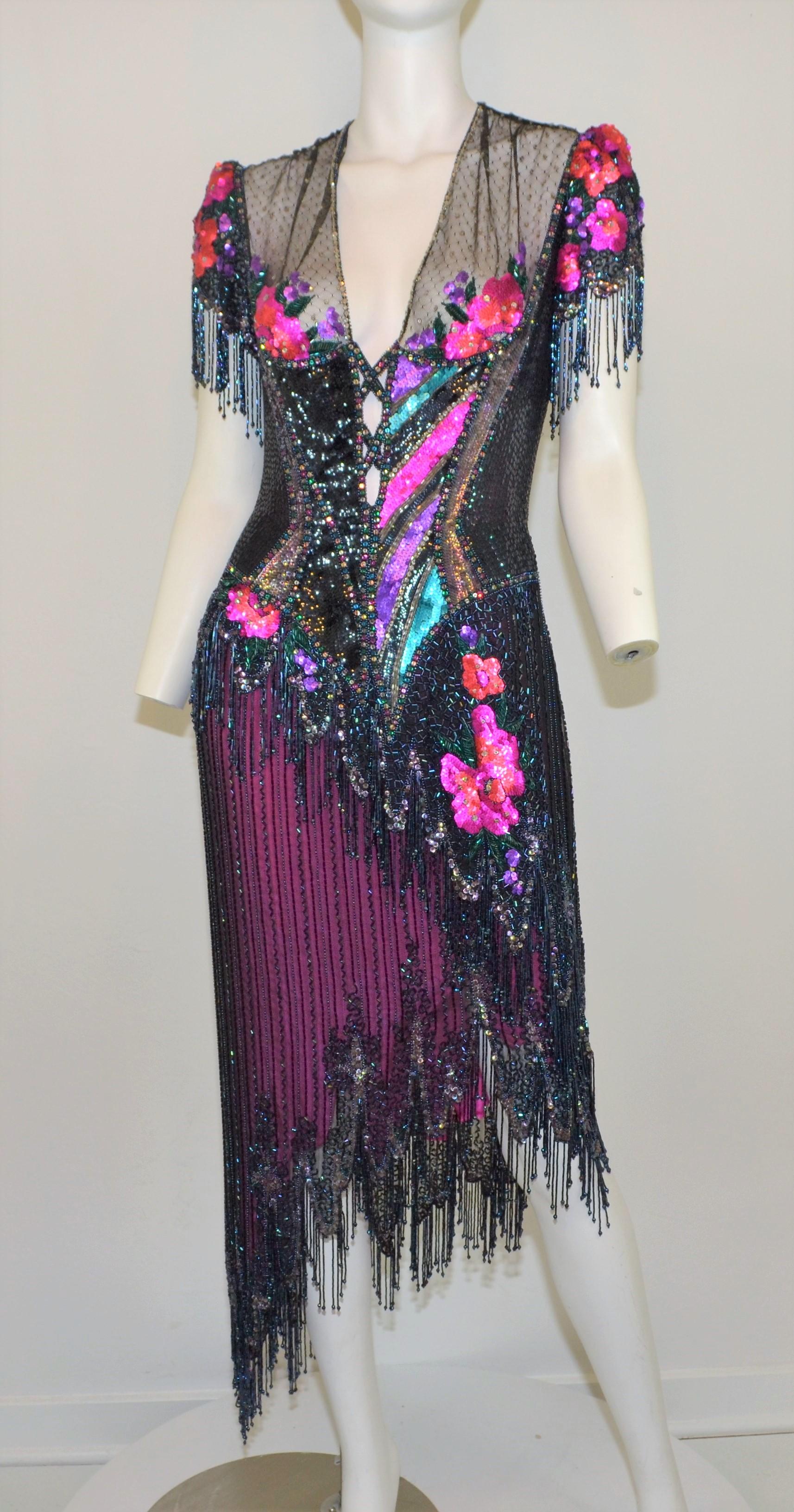 Bob Mackie 1970's Fringe Beaded Evening Dress -- Featured in a variation of jewel tones throughout with a fringed, asymmetric hem design. Dress has a floral motif, mesh back with a zipper and hook-and-eye fastening. Dress is in great vintage