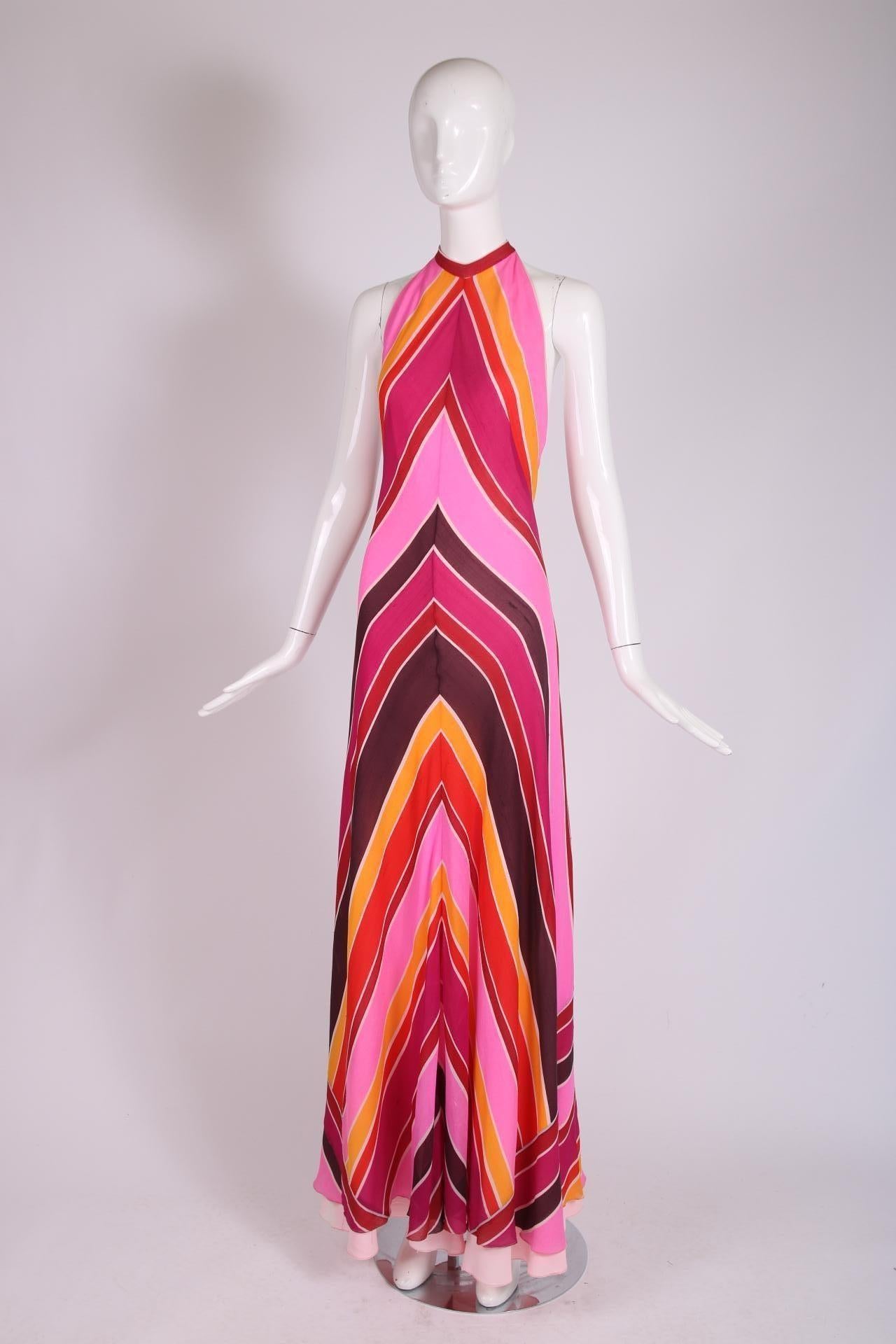 1970's Mackie & Aghayan pink, fuchsia, red, orange and white chevron stripe halter gown with an open back and hem that flares at the bottom. Fabric is mildly sheer and is lined at the interior with what could be pink crepe. The gown fastens at the