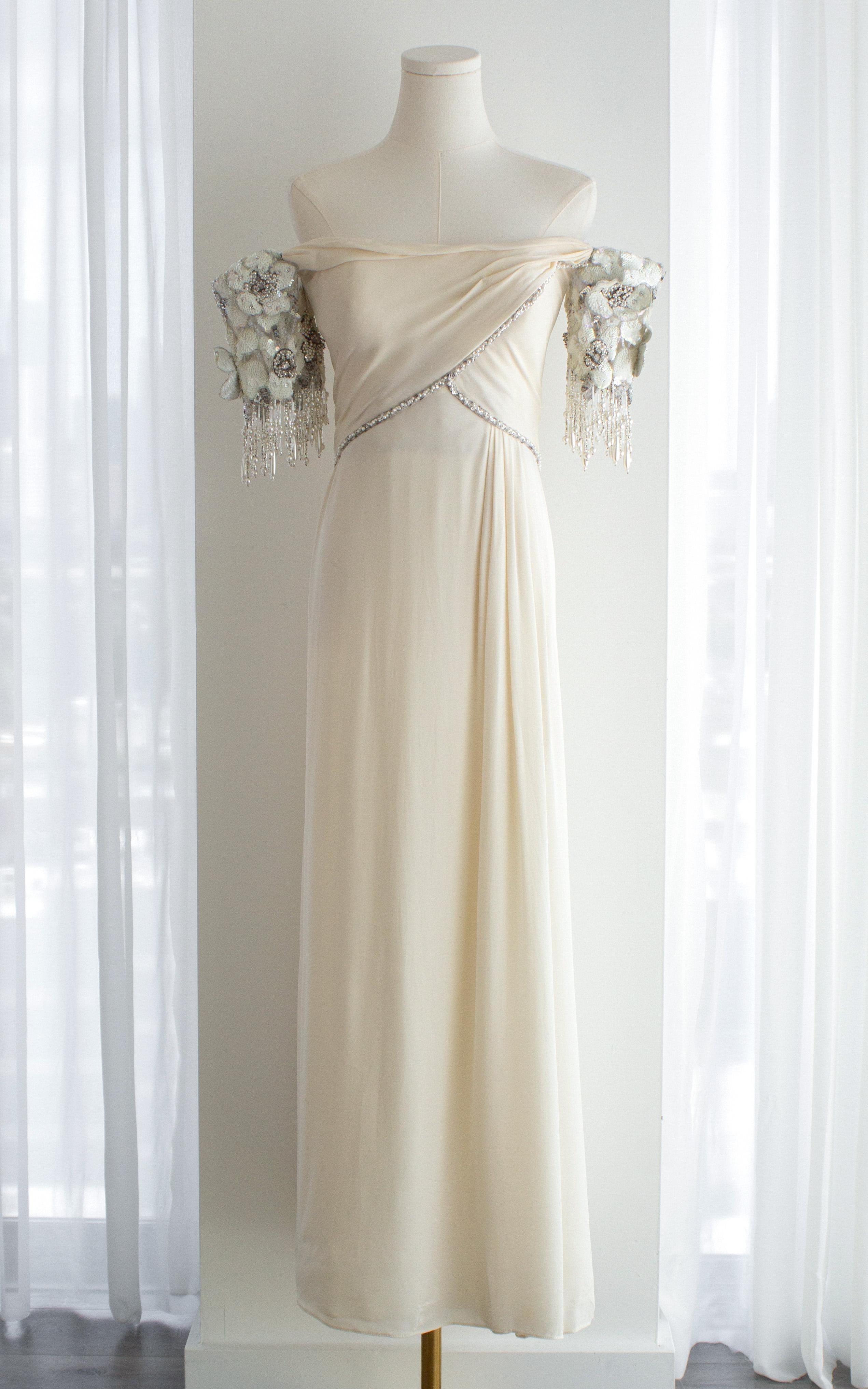 An extraordinary piece of vintage glamour by Bob Mackie, this off-white gown is a rare example of his romantic, red carpet-ready eveningwear. Crafted from fluid silk crepe, the dress features a graceful off-the-shoulder neckline with sculptural