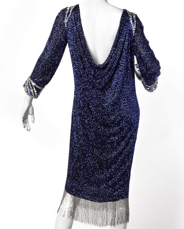 Stunning cobalt blue glass beaded cocktail dress by Bob Mackie. This heavily beaded and sequin embellished formal features silver Art Deco inspired keyhole collar and arm cuffs, a plunging draped two-layer back, and swinging silver beaded fringe