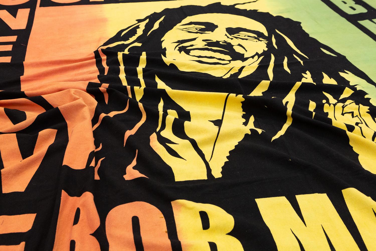 This is a 21st-century textile made using a printed stamp technique and was woven in America. It depicts Bob Marley and one of his most famous and influential songs “one love” and is made up of three different colors starting on the left with orange
