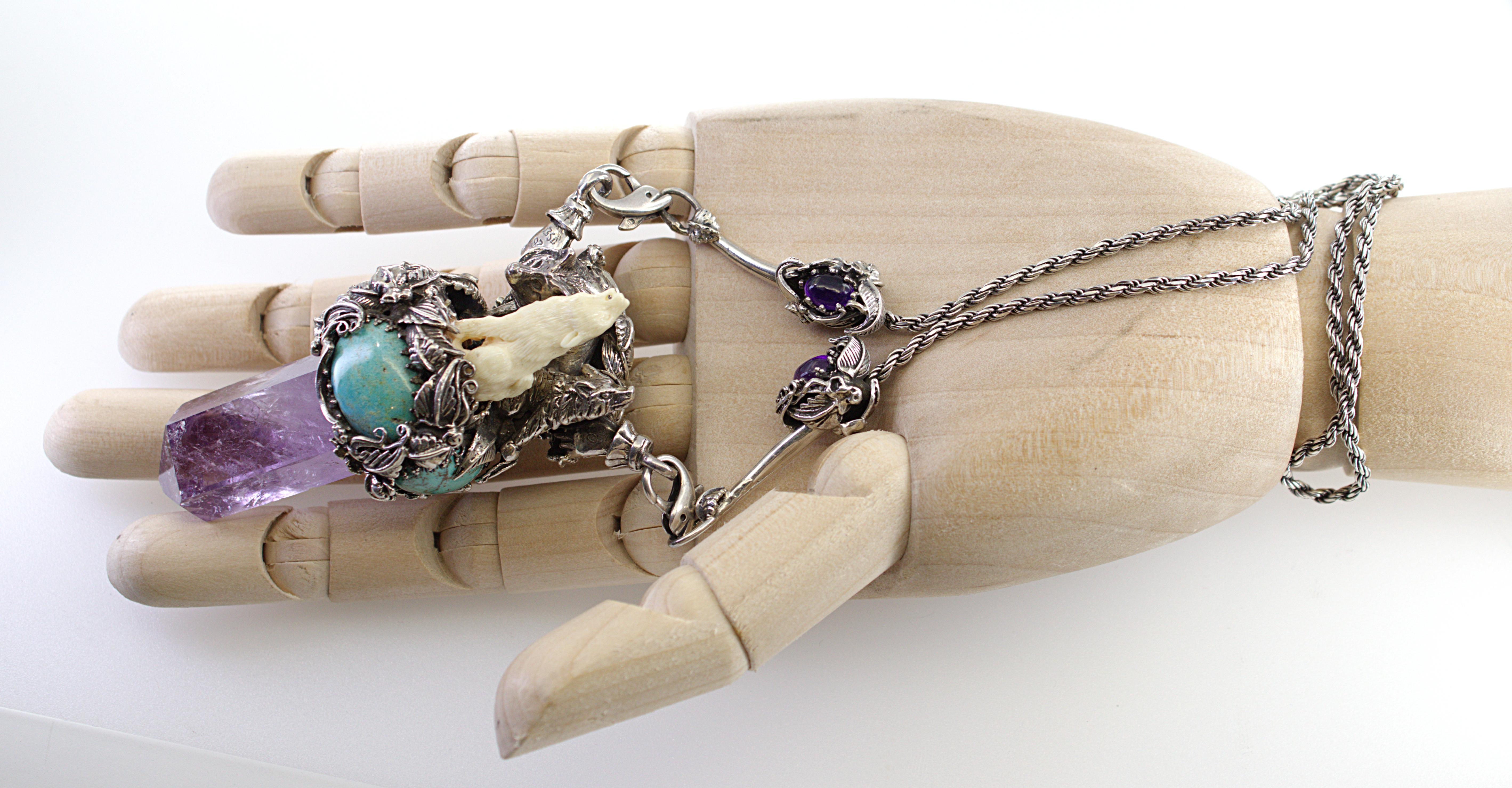 Featuring (1) natural amethyst crystal, 43.9 X 19.6 X 15.2 mm, accented by (5) oval turquoise cabochons, 19 X 16 mm to 14 X 10 mm, surmounted by a carved mammoth ivory wolf, set in a silver, double sided, 3-D mounting, depicting a mother wolf with 2