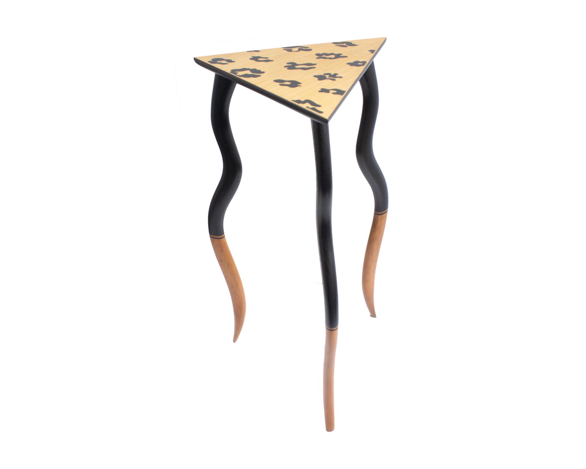 A 1980s or early 1990s Postmodern wooden table designed by American artist and designer Bob Trotman (born 1947). Titled Dancing Table, this wooden accent table has a triangular top and three wavy legs. The table has a leopard spot design to the top