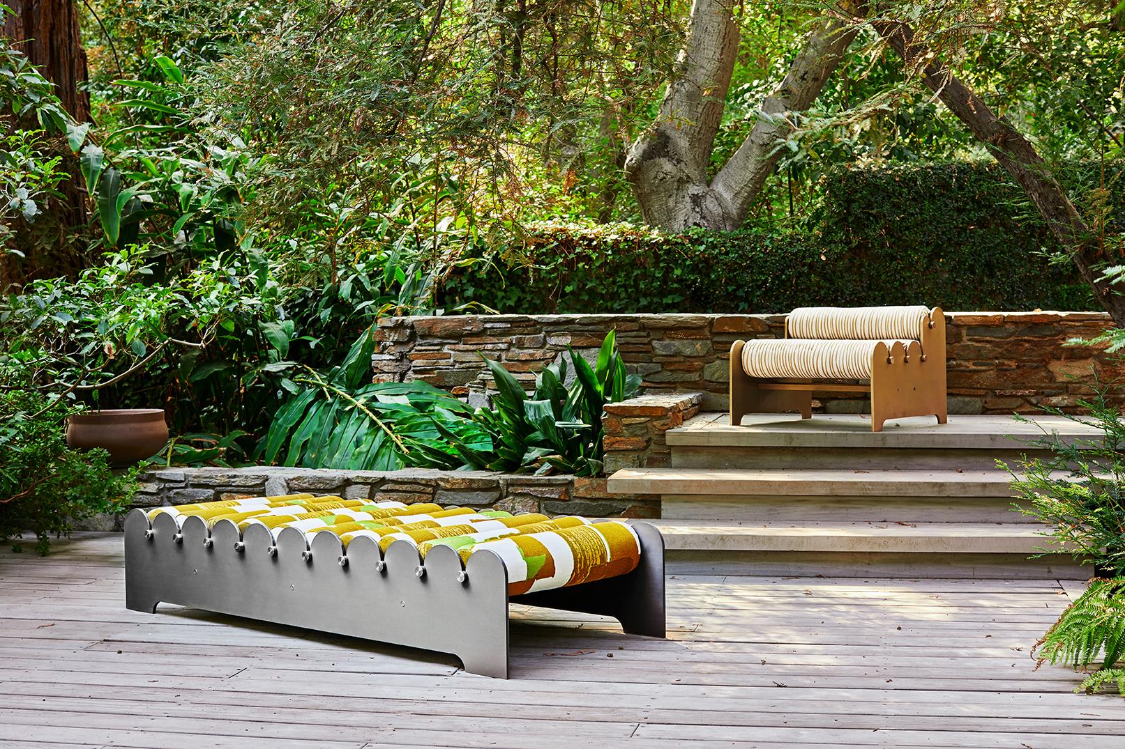 A series of bolsters are threaded between two aluminum rails that evoke the waves of the Pacific. The Bobbin bench is suitable for indoor or outdoor use. Stainless steel rods thread through each outdoor quality cushion and connect the patinated