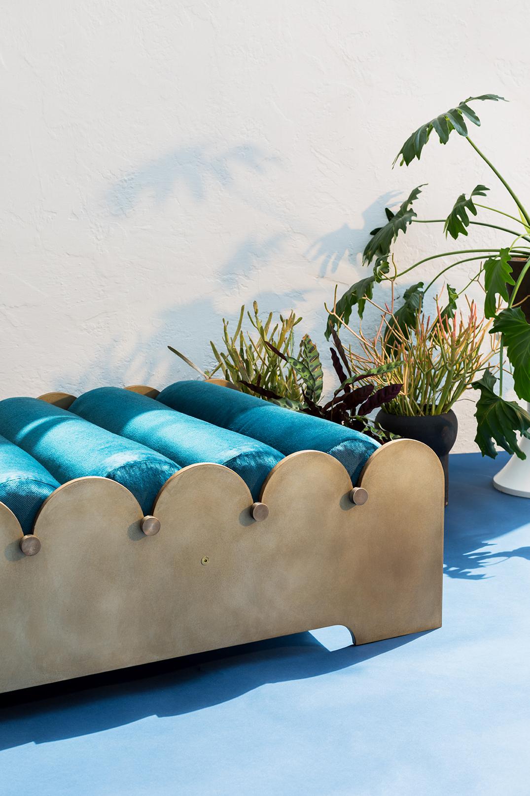 A series of bolsters are threaded between two aluminum rails that evoke the waves of the Pacific. The Bobbin bench is suitable for indoor or outdoor use. Stainless steel rods thread through each outdoor quality cushion and connect the patinated