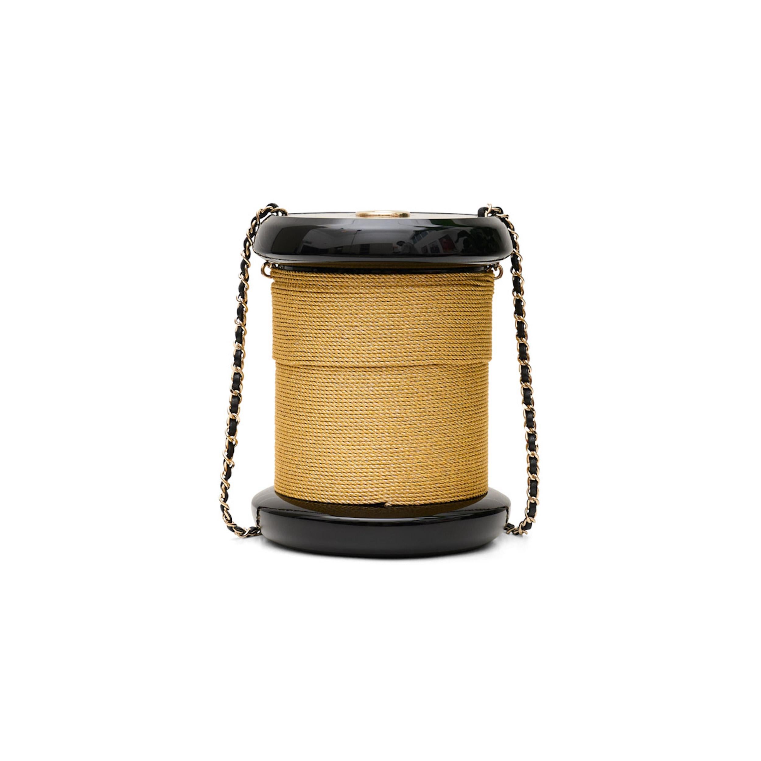 This CHANEL Plexiglass Bobbin Minaudière Clutch is both authentic and stylish. The beautiful black plexiglass is shaped like a spool of cotton thread, with a gold rope wrapped around it. The detachable gold plate and leather shoulder strap add a
