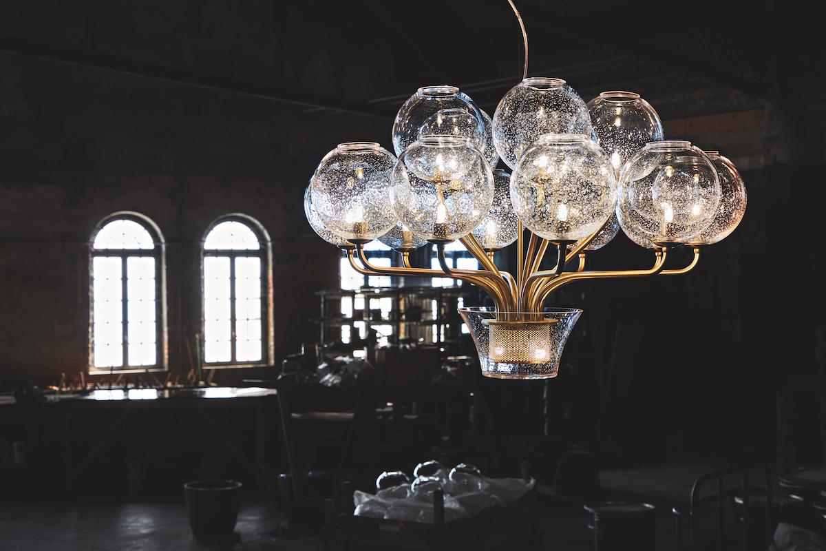 Lustre composé d'une sphère décorée en verre clair et lait de Murano avec des décorations opaques grises sur des bras en métal avec des finitions en chrome satiné qui convergent dans un élément central en verre.


Carlo Moretti : Une usine